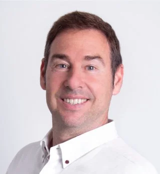 Hombre sonriendo con cabello castaño y camisa blanca, fondo blanco.