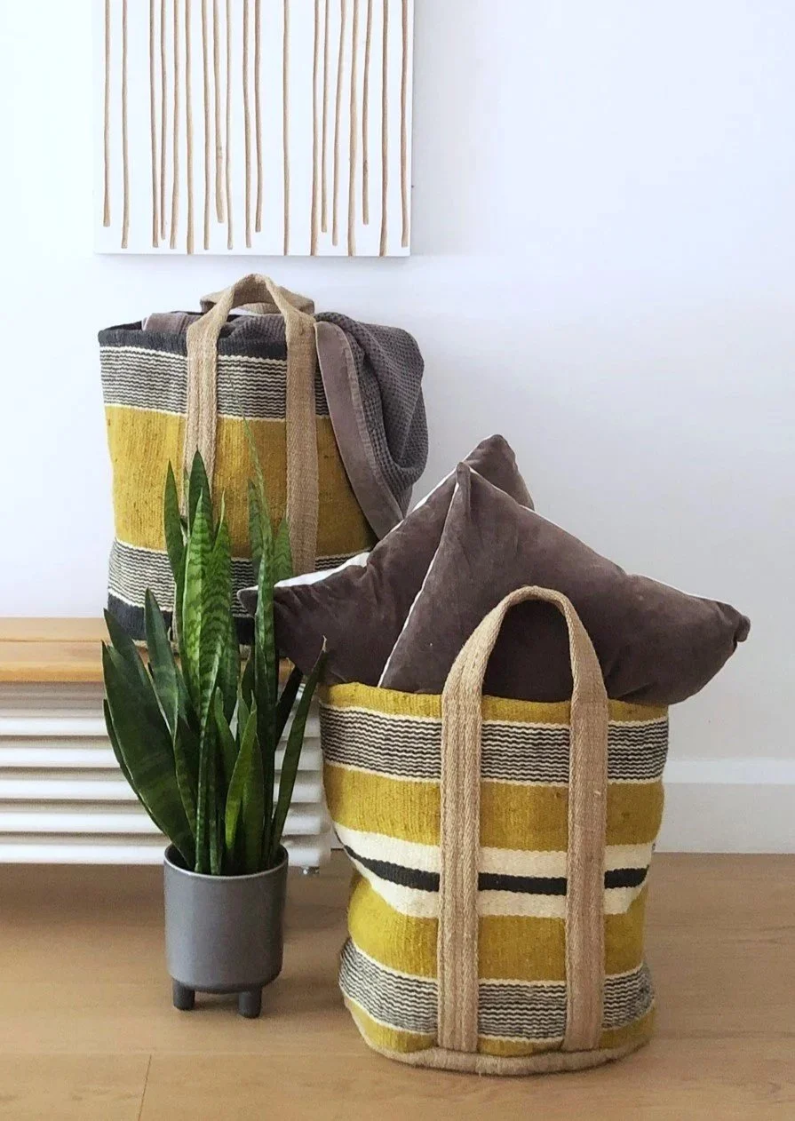 Decorative striped yellow, black, and beige tote bags with brown pillows, a potted snake plant, and wall art with vertical beige lines on a white wall.