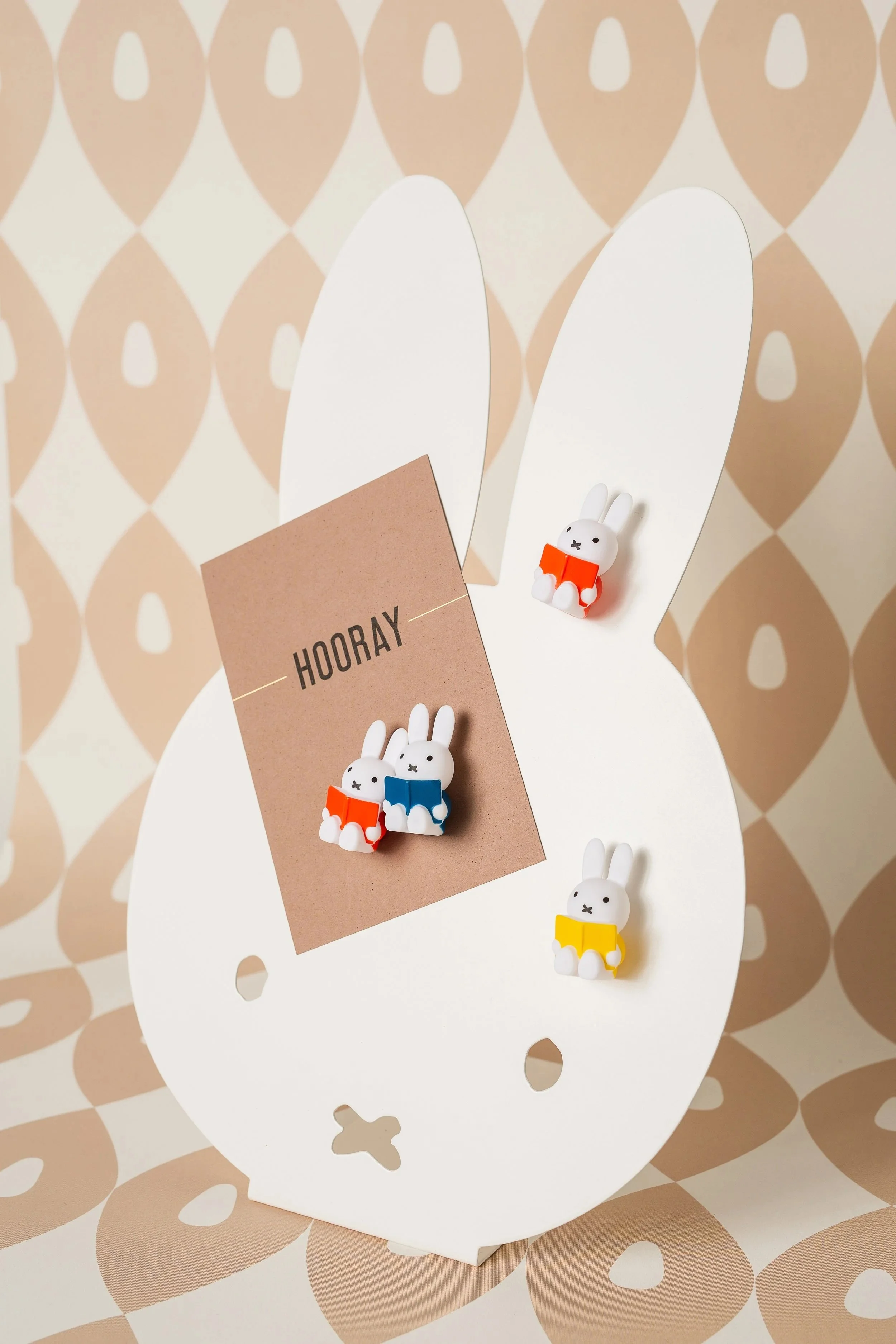 White bunny-shaped display with three small bunny figurines in red, blue, and yellow outfits, and a brown card with the word 'HOORAY' attached to the display.