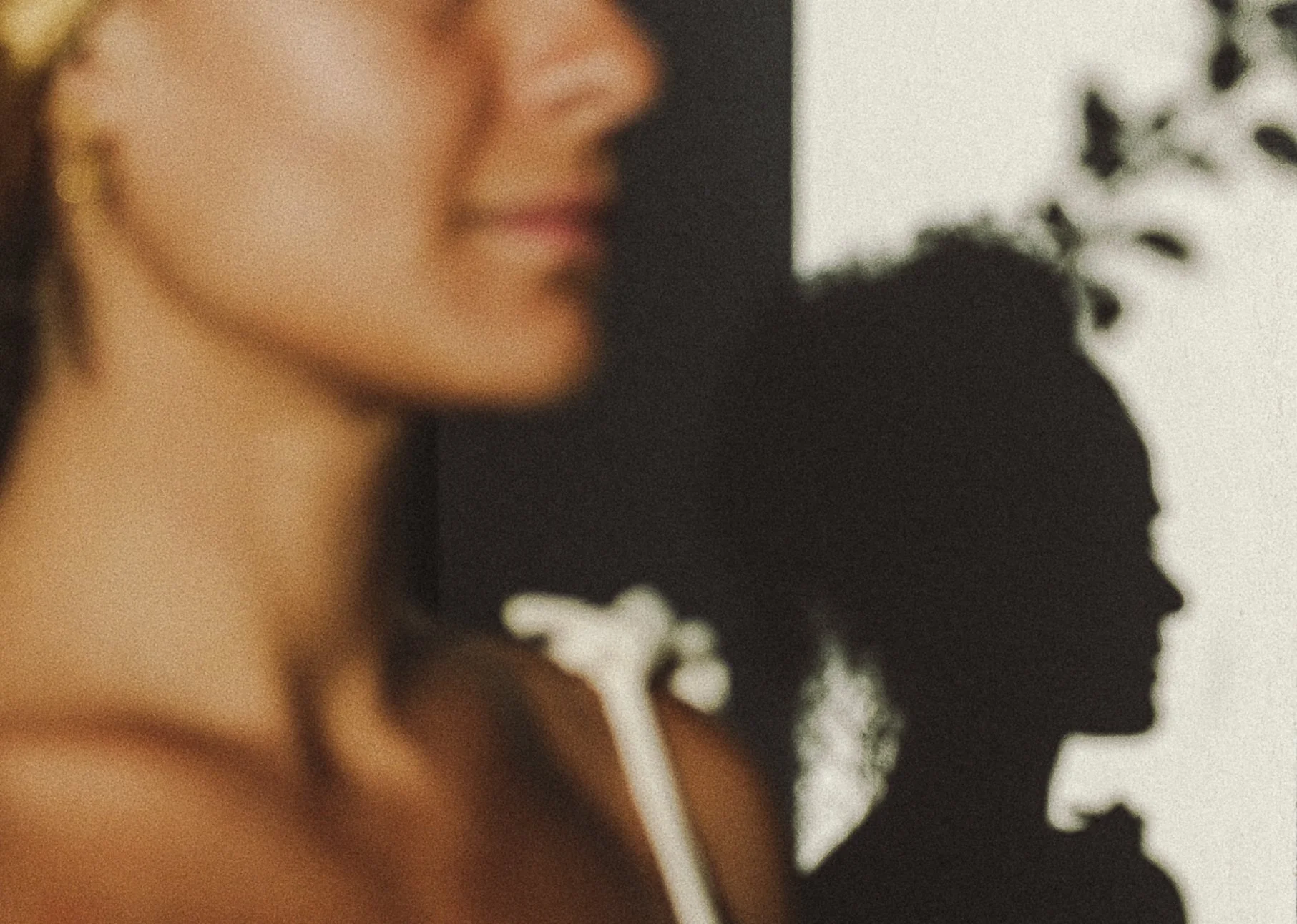 Close-up of a woman's face and shoulder with a silhouette of her profile cast on a wall behind her.