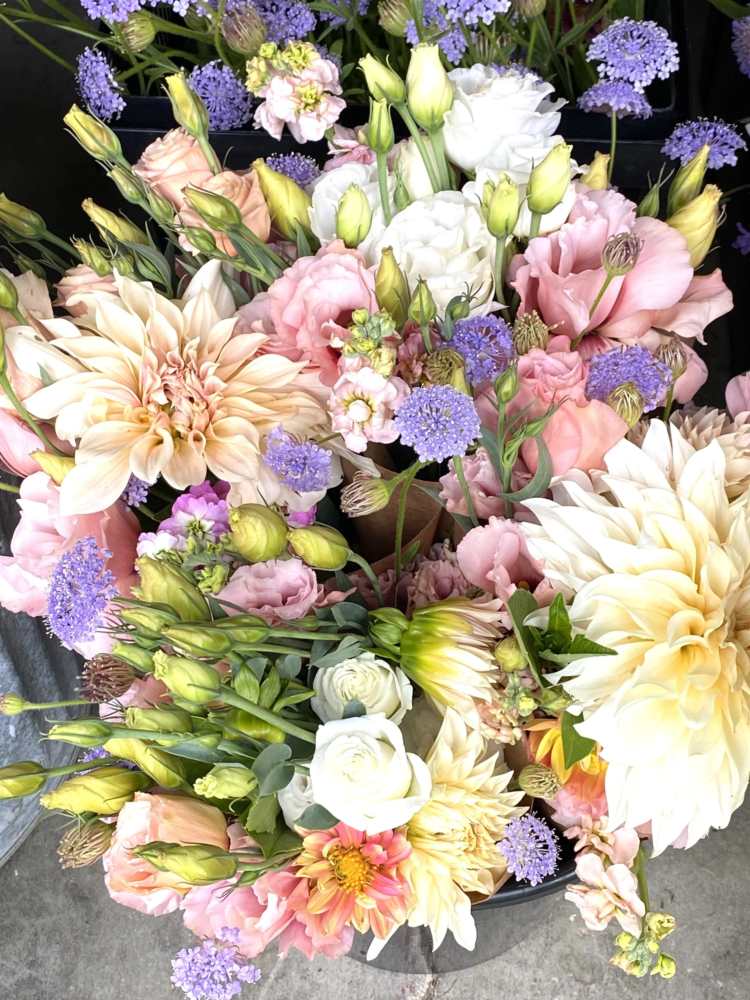 A colorful floral arrangement with pink, white, cream, and purple flowers, including dahlias, roses, lisianthus, and lavender.