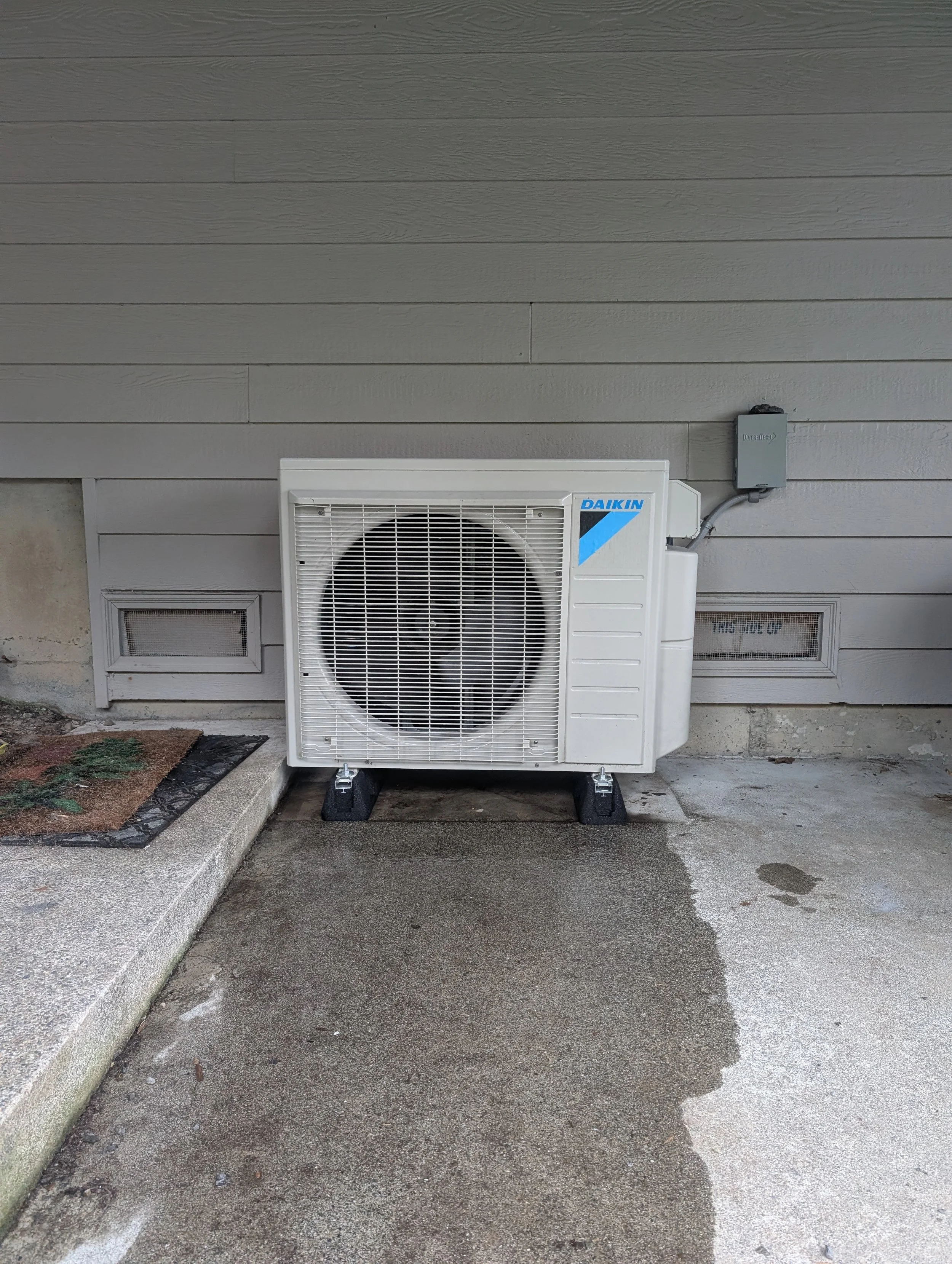 Outdoor air conditioning unit installed next to a house wall.