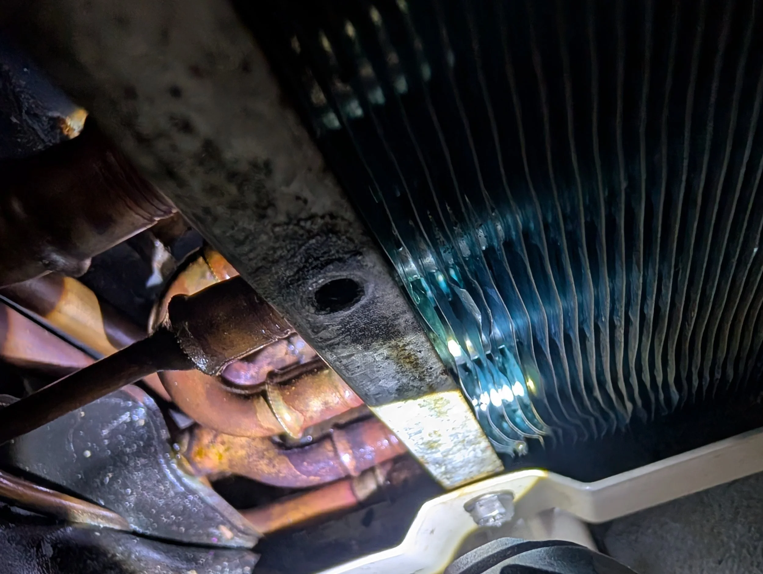 Close-up of an air conditioners heat exchanger, showing rust and leaks with traces of oil and refrigerant.