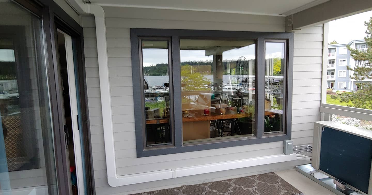 Balcony with a sliding glass door, a large window overlooking a body of water, an outdoor air conditioning unit, and a patterned rug.