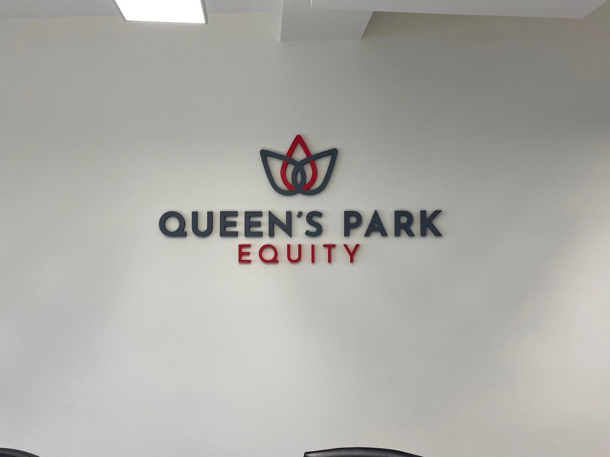 A wall with a logo of a stylized lotus flower in black and red, and the text 'Queen's Park Equity' in black and red letters.