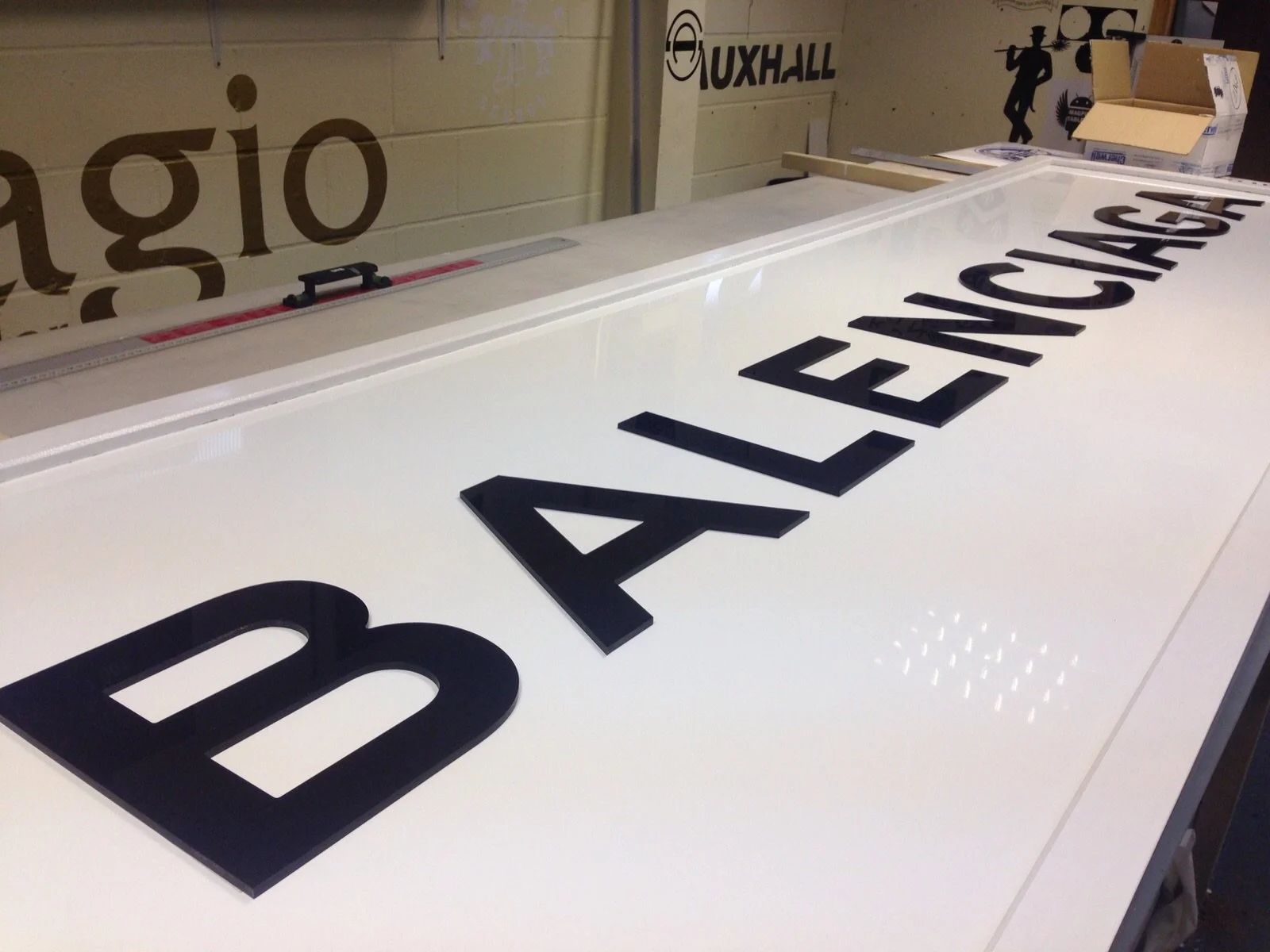 Close-up of a white sign with black 3D James A. Leninger text on it, placed on a worktable in a workshop.