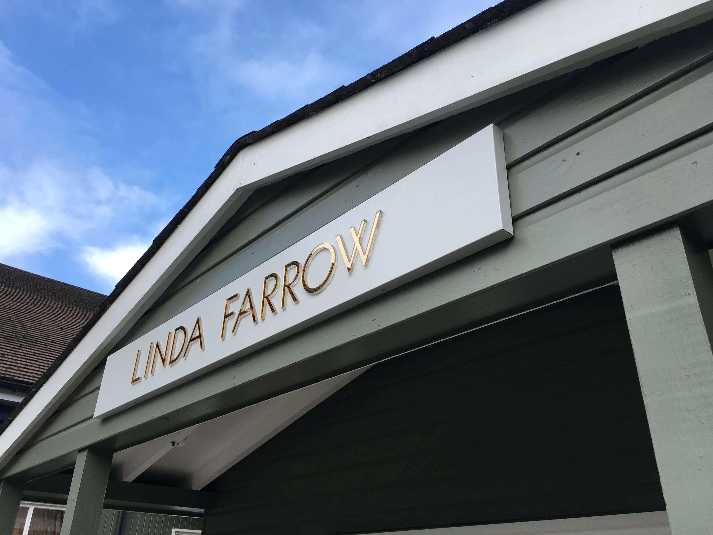 Sign reading 'Linda Farrow' on the exterior of a building with a cloudy sky in the background.