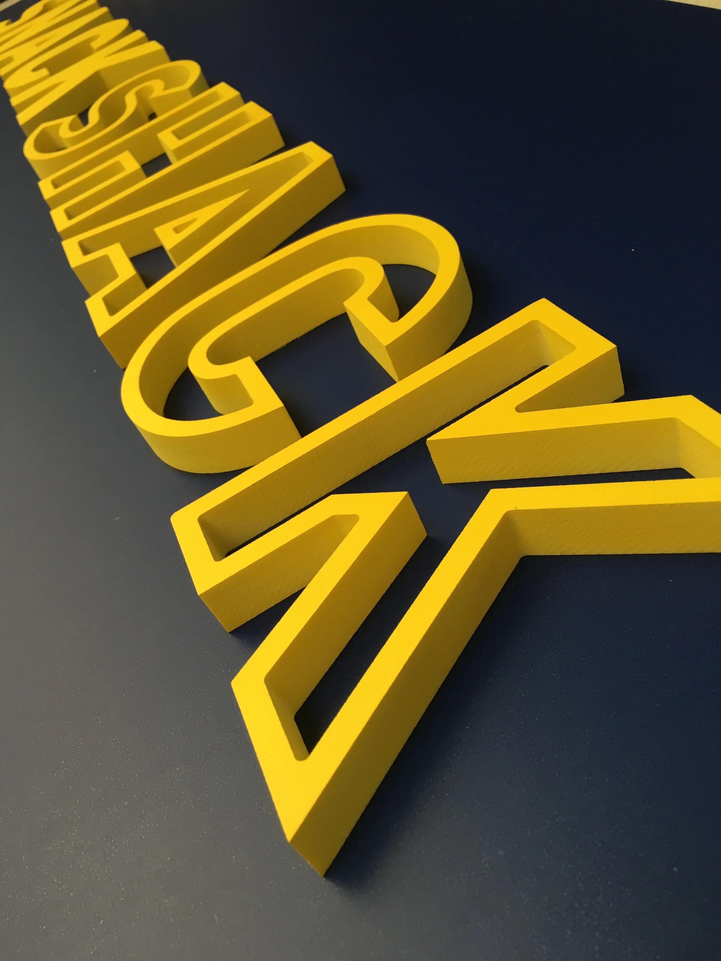 Close-up view of yellow 3D letters on a black surface.
