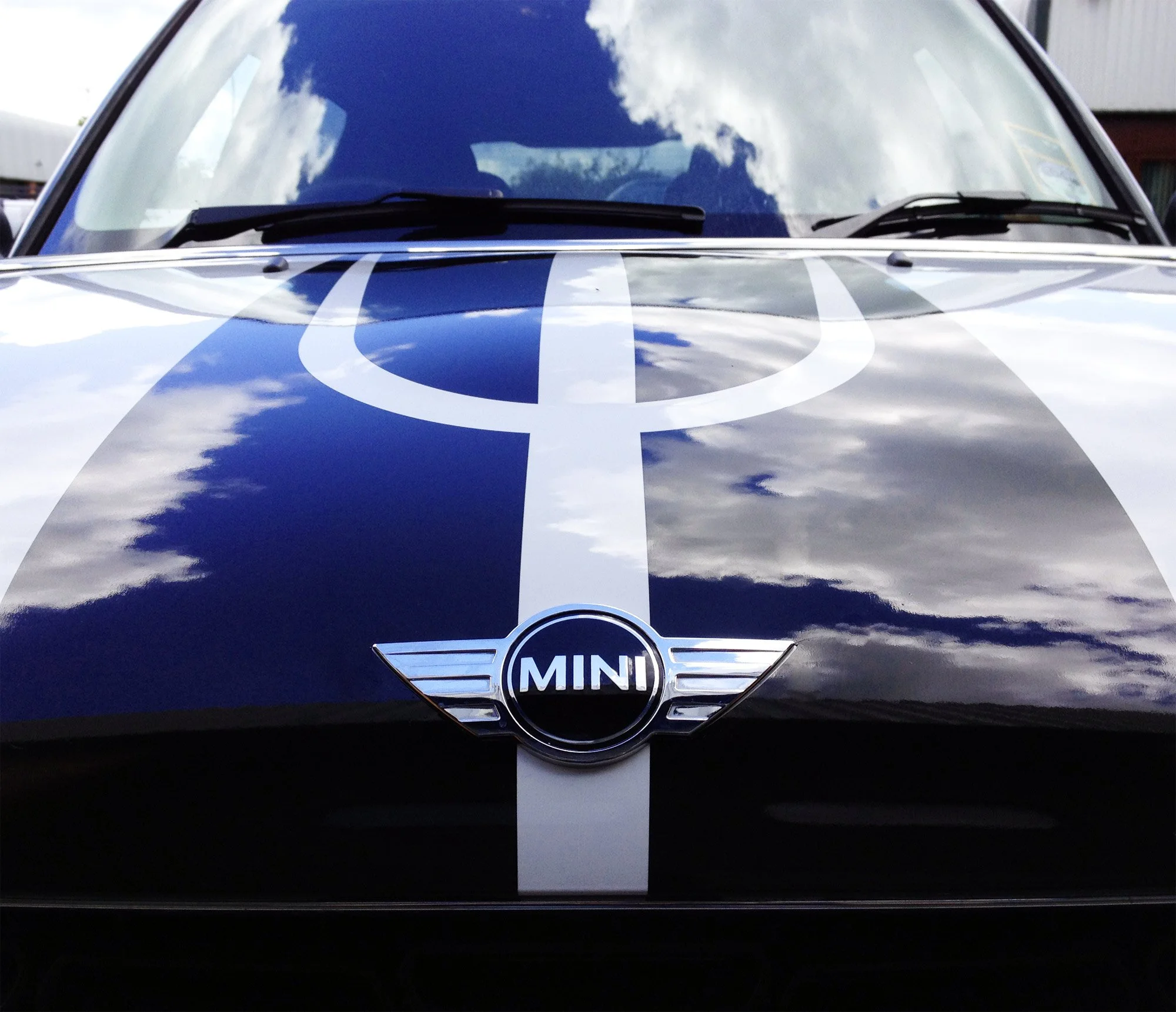 Close-up of the front of a MINI car with a black hood, white racing stripe, and MINI logo badge.