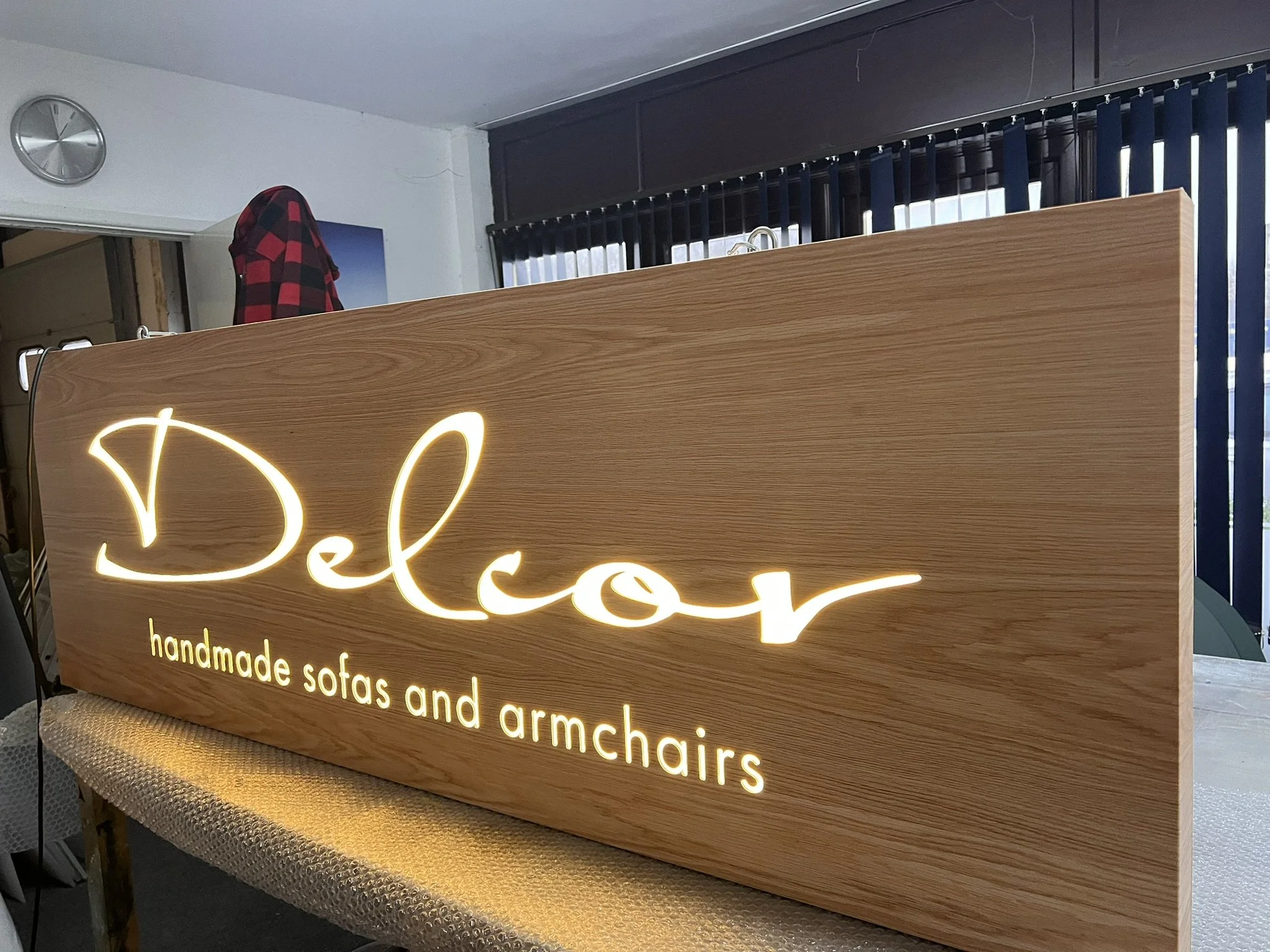 Wooden sign with illuminated cursive text reading 'Decor' and smaller text below stating 'handmade sofas and armchairs' in a furniture store.