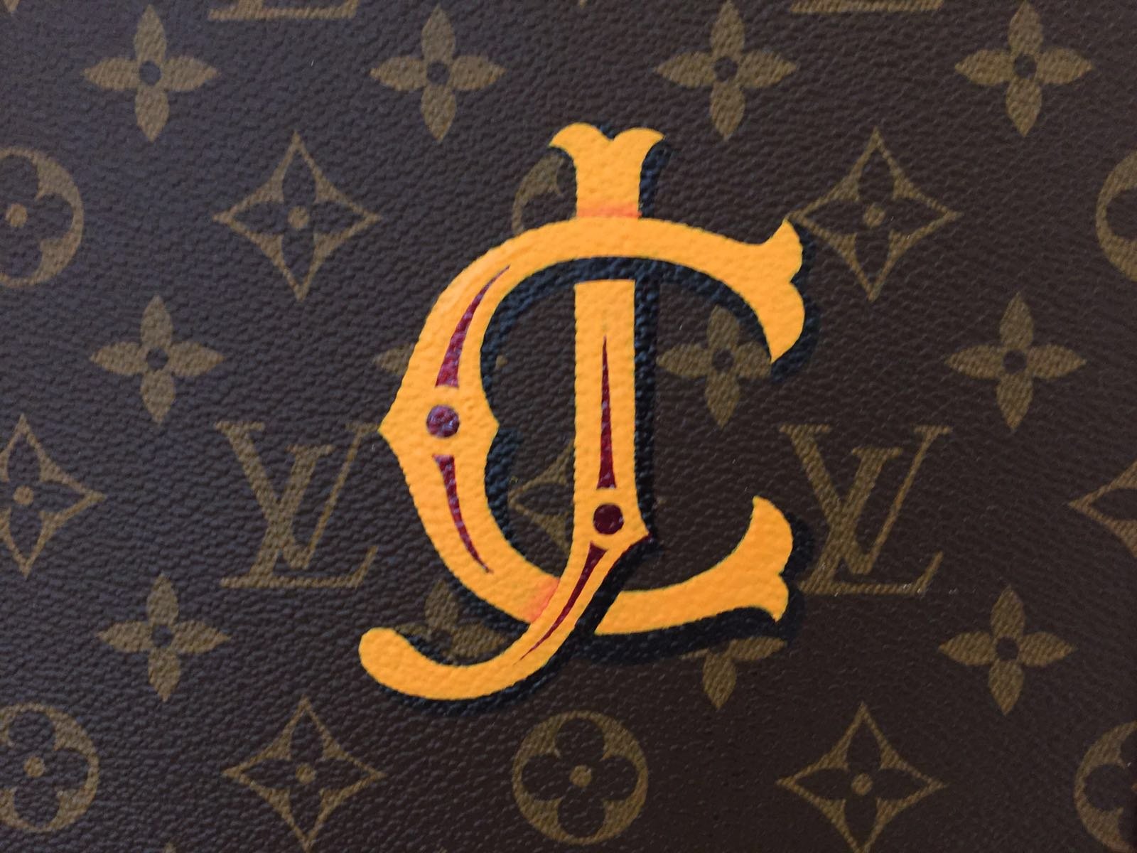 Close-up of a monogrammed Louis Vuitton leather surface with an embroidered yellow and red monogram and the brand's signature pattern.