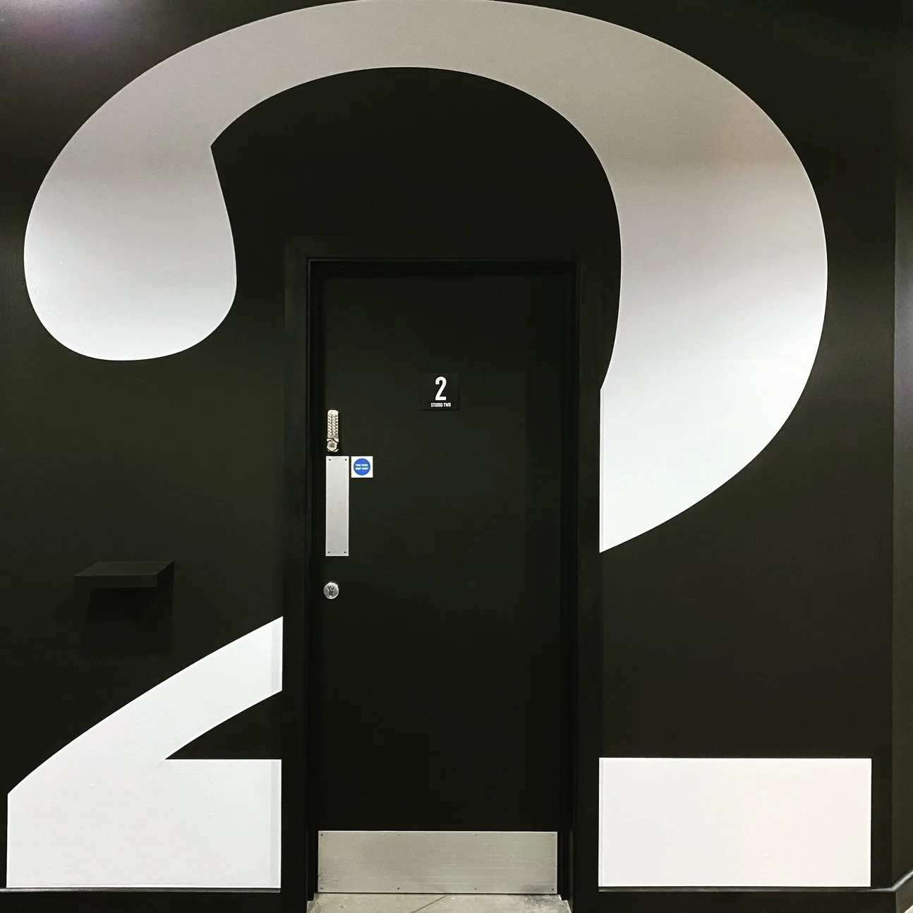 A black door marked with the number 2 on a wall decorated with large black and white abstract numbers 2 and 1.