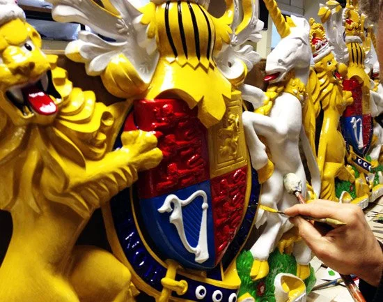 Person painting a detailed, colorful dragon and lion sculptures, featuring a shield with white swan and harp symbols, in an art studio.