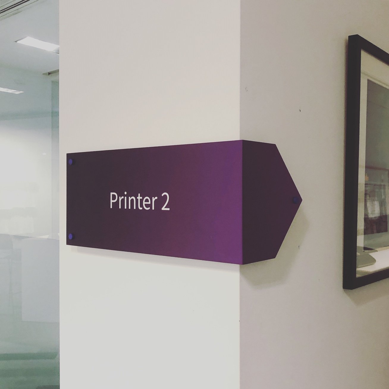 Purple directional sign on white wall reading 'Printer 2' with a purple arrow shape pointing right.