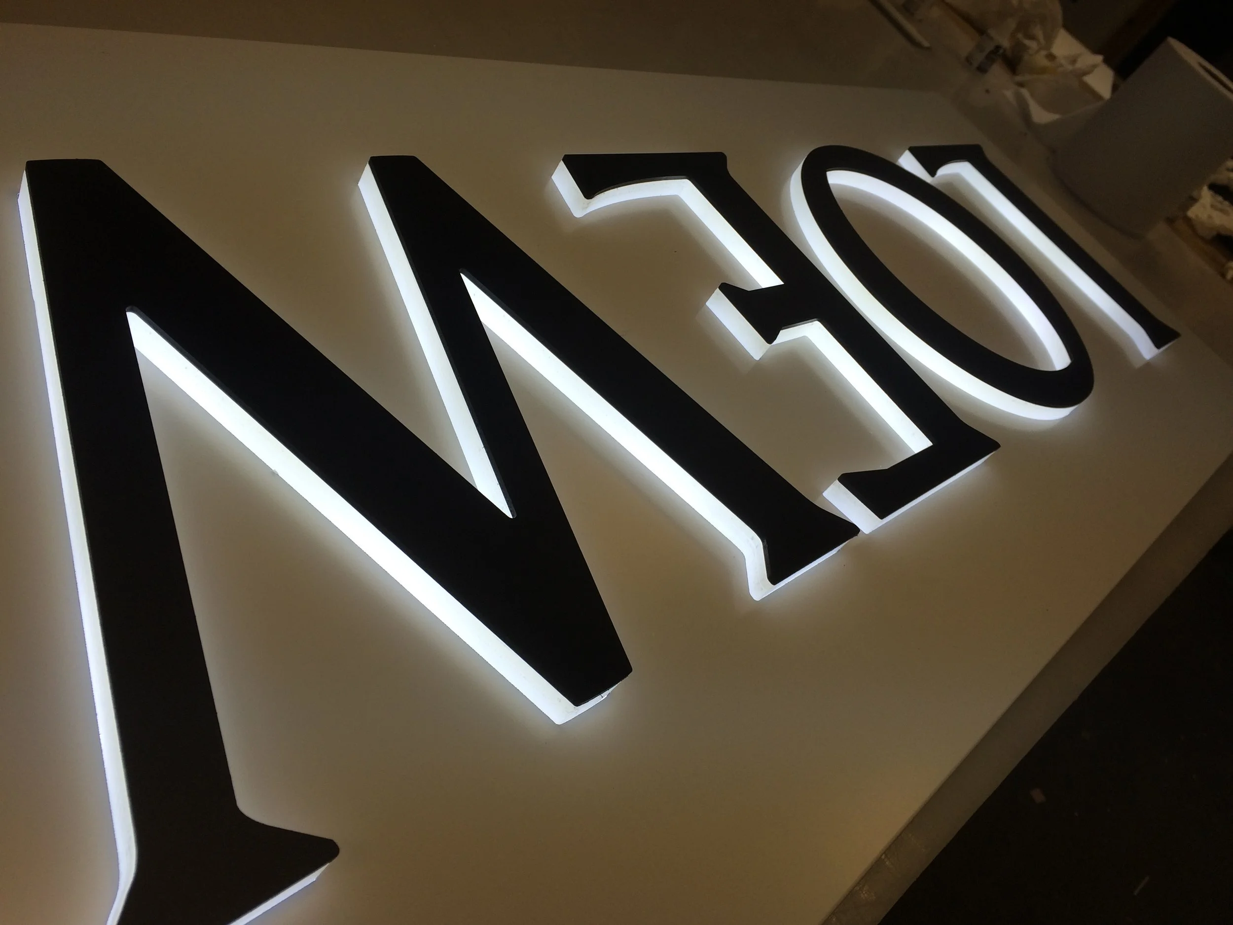 Close-up of illuminated black and white sign with the letters 'N' and 'O' on a light-colored surface.