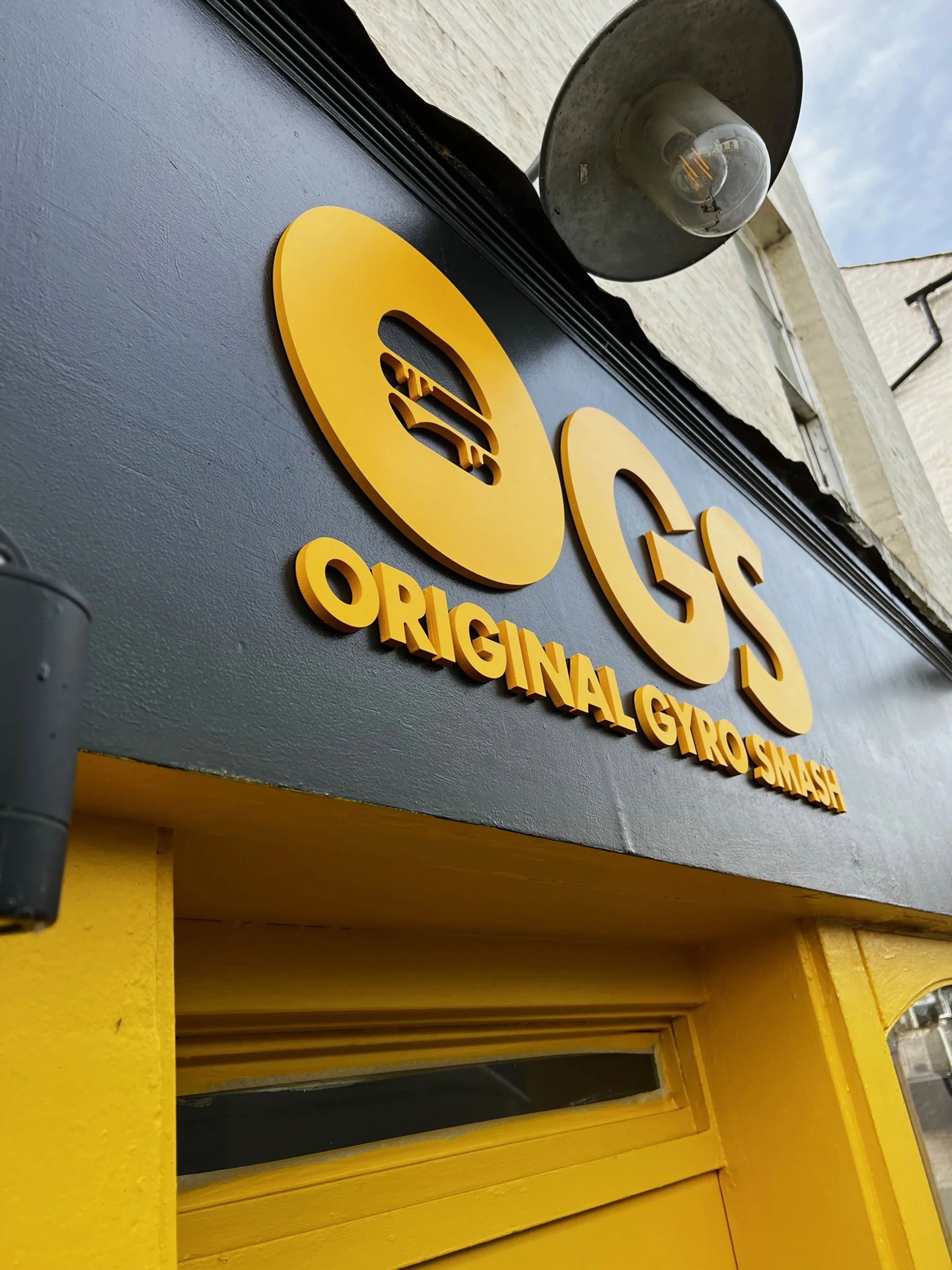 Close-up of a sign with a Gs and an icon of a gyro sandwich, with the text 'Original Gyro Smash' below.