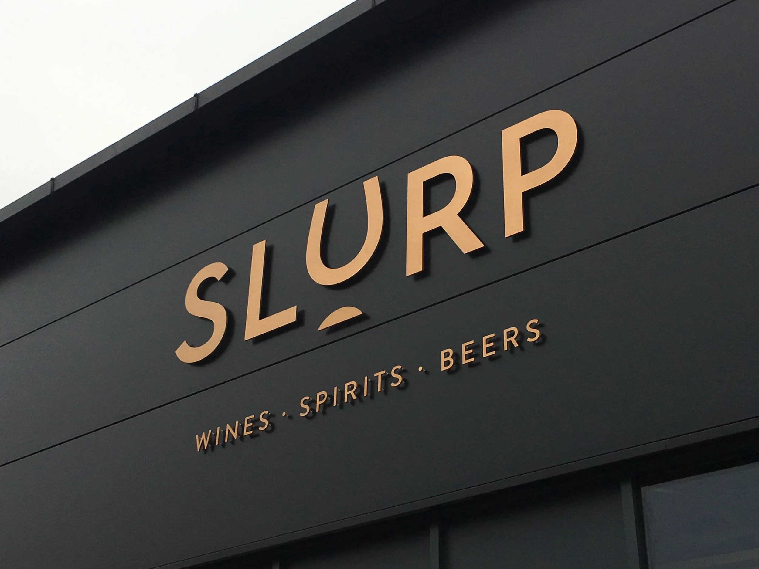Storefront sign reading 'SLURP' with smaller text below saying 'WINES • SPIRITS • BEERS'