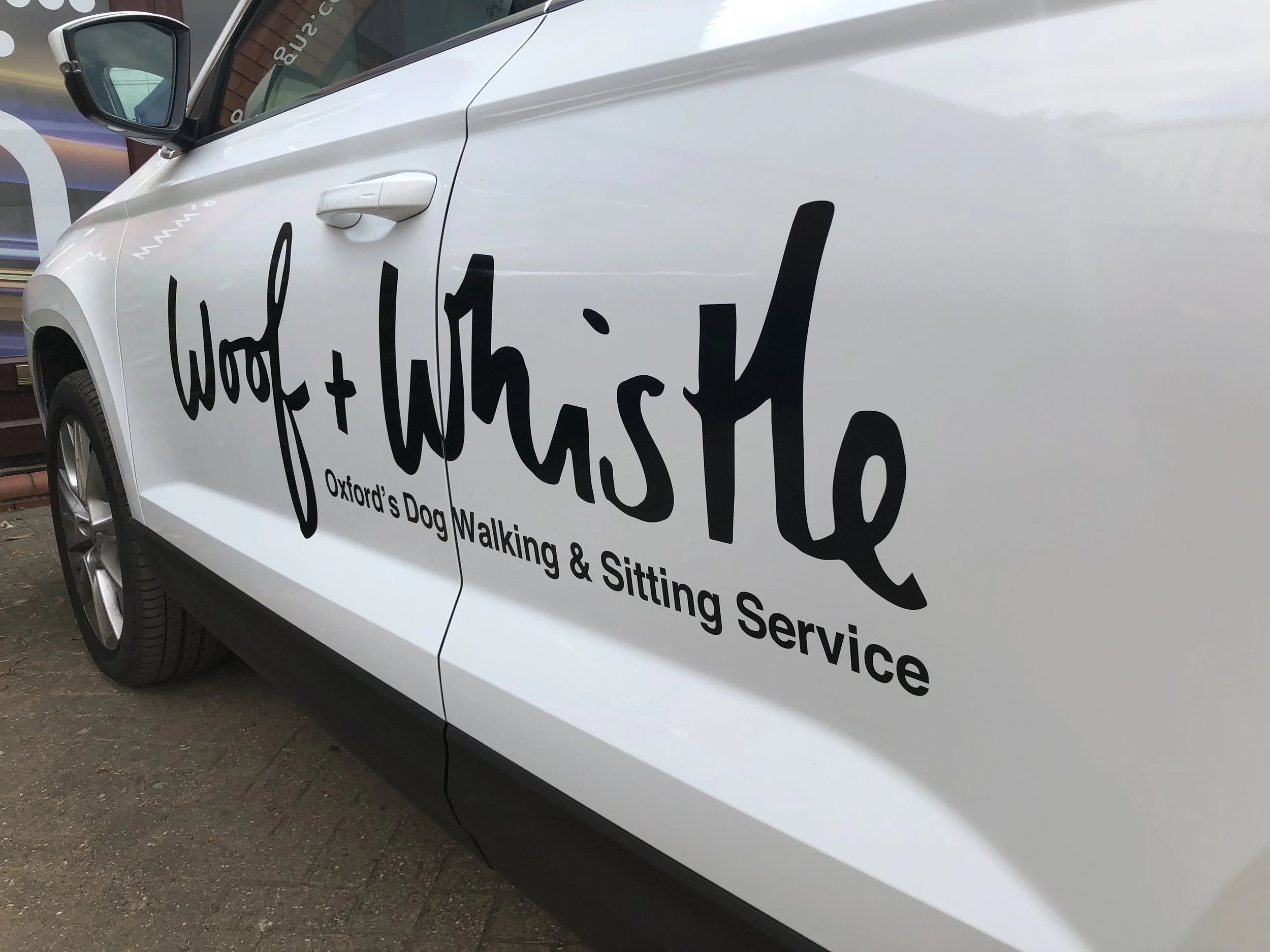 White vehicle with black text advertising Woof & Whisk, a dog walking and sitting service in Oxford.