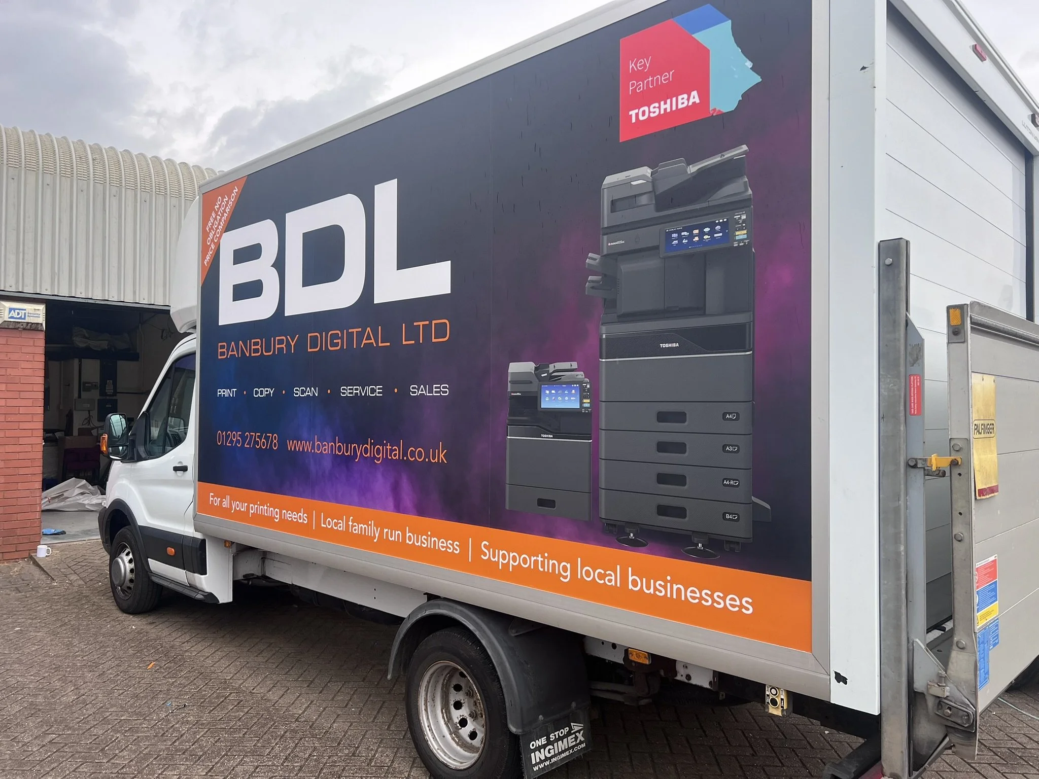Advertisement on the side of a delivery truck for Banbury Digital Ltd, a business supporting local businesses with printing, copying, scanning, and servicing products. The ad features images of Toshiba multifunction printers and the company's contact details and website.