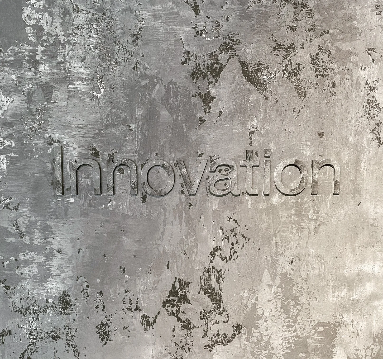 Metal wall with the word 'innovation' cut out, featuring a textured, distressed surface.