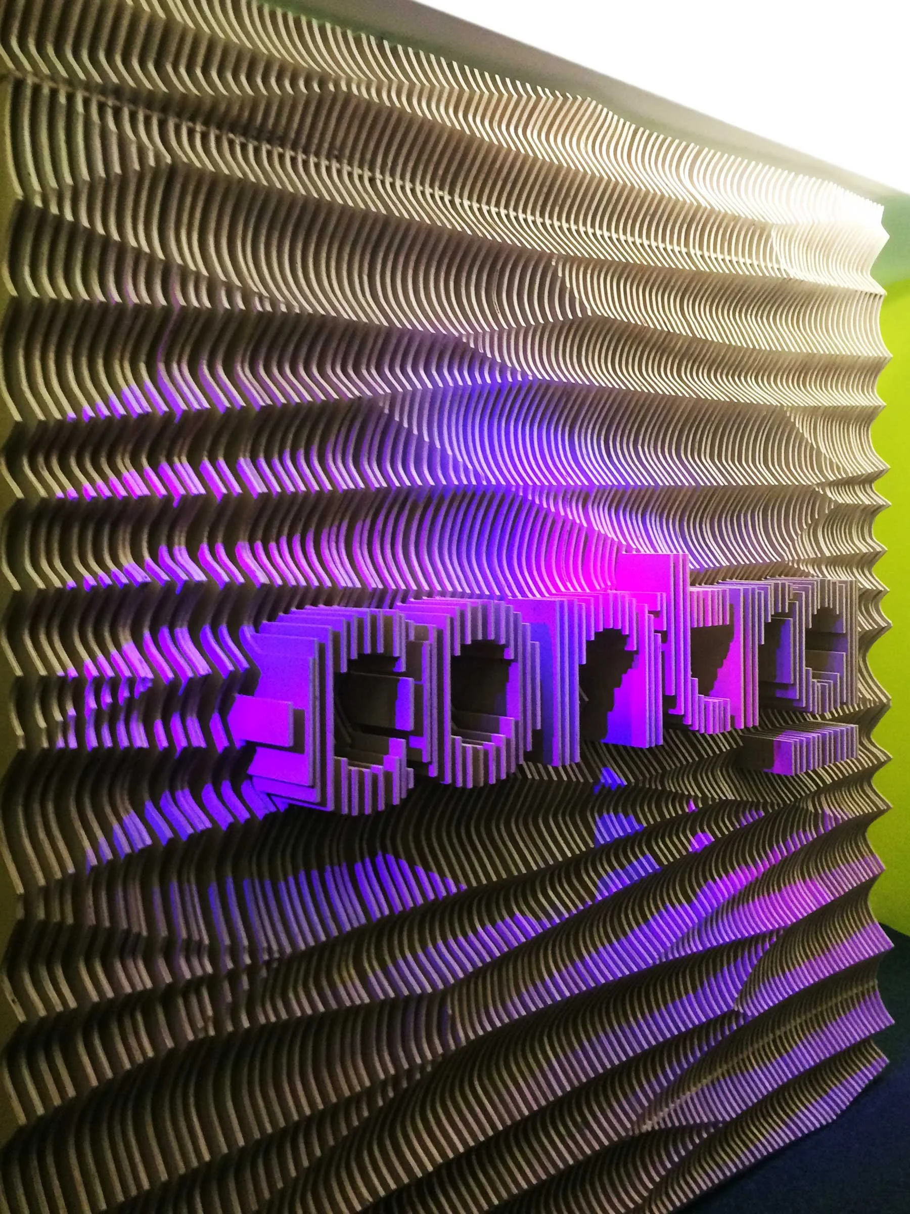 Decorative wall with stacked, curved, black layers and illuminated purple letters spelling 'CODE' in the center.