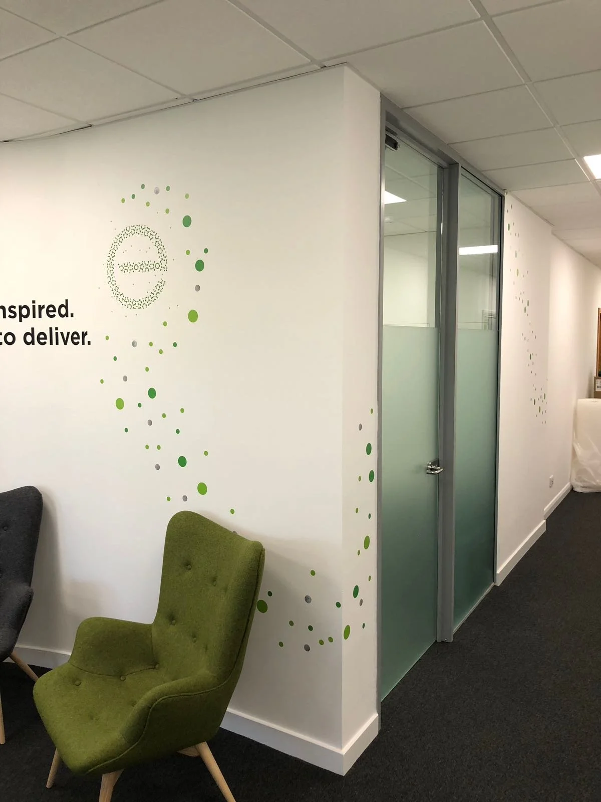 Office interior with white walls, a glass door, and a green upholstered chair.