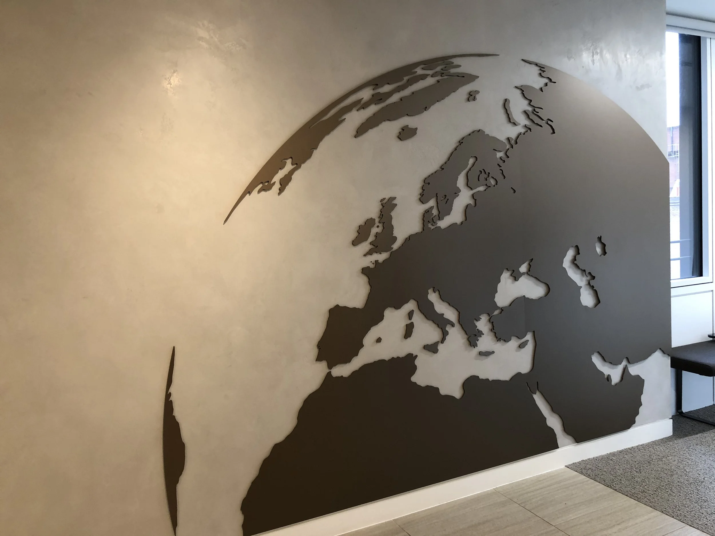 Decorative wall art of a world map silhouette in a modern interior space near a window.