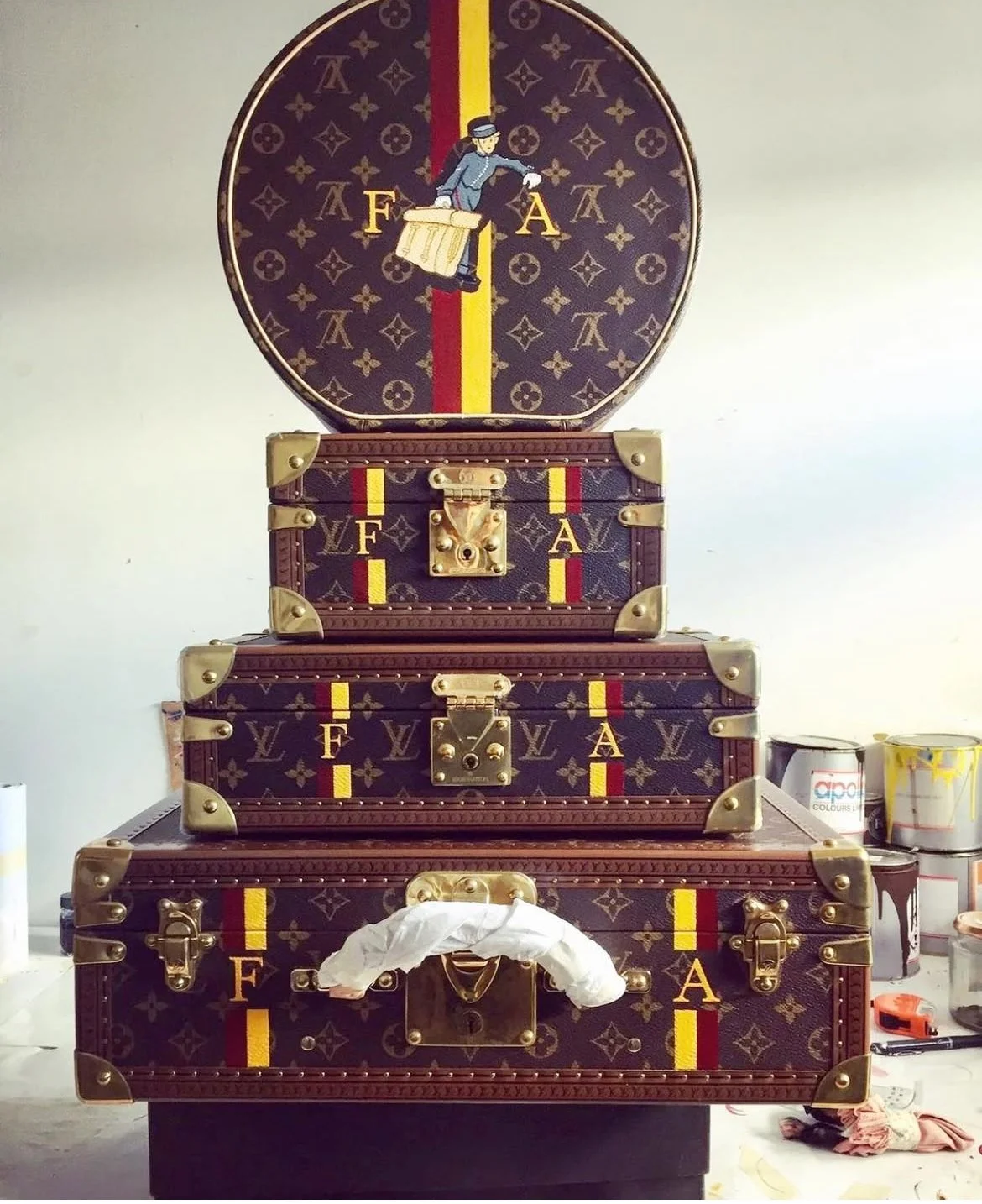 Stacked vintage Louis Vuitton suitcases and a clock with a Louis Vuitton pattern and a woman figure on its face.