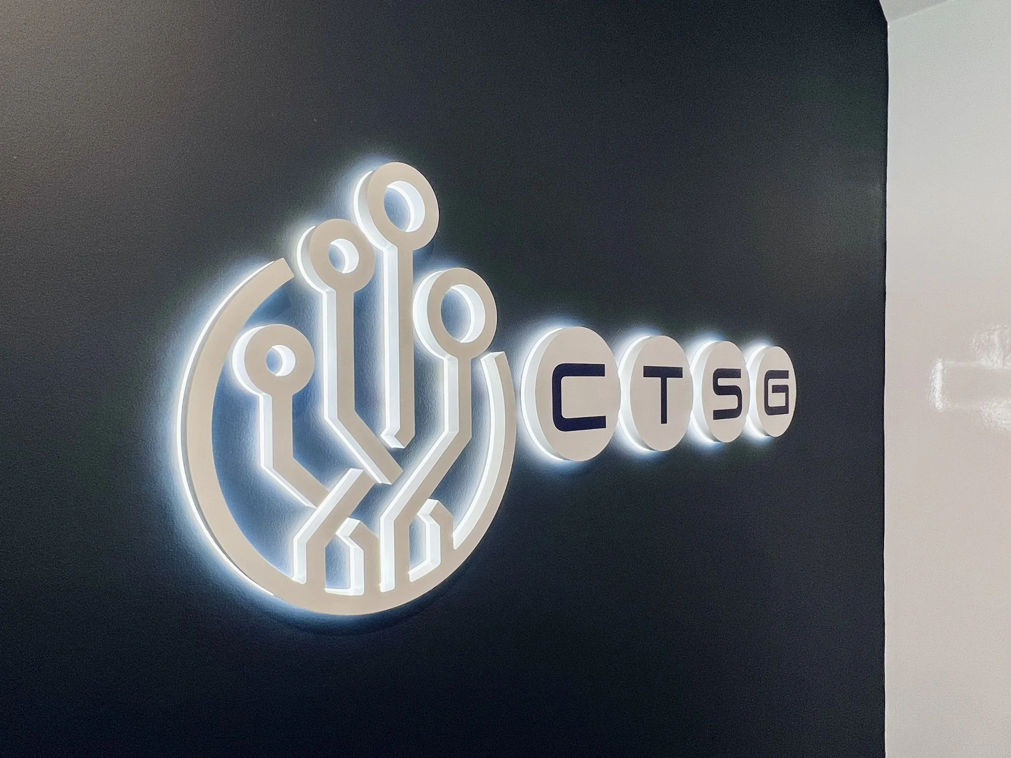 Illuminated logo on a dark wall displaying a circuit-like design and the text 'CTSG' in block letters.