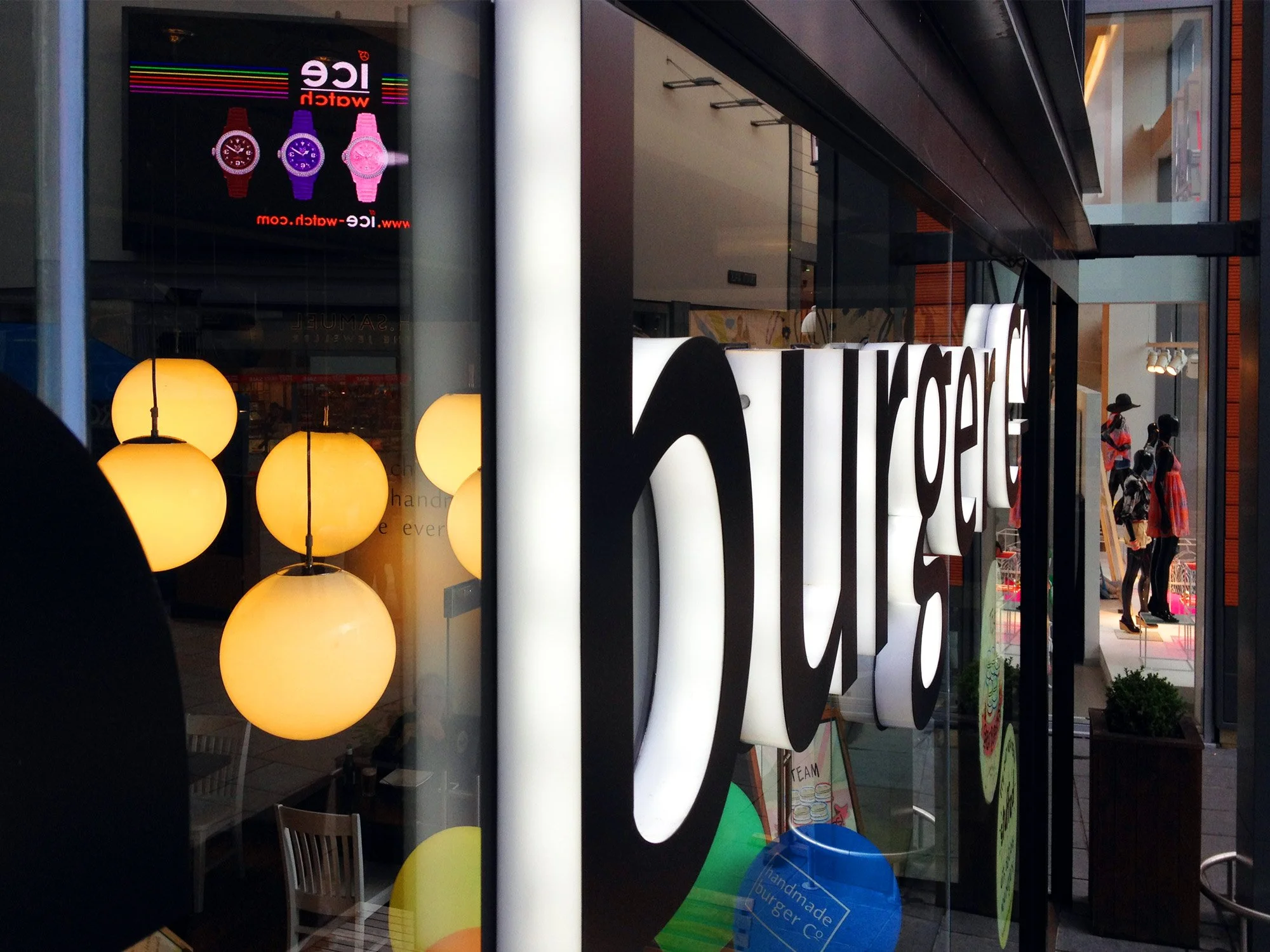 Storefront window with illuminated sign reading 'Kale' and a display of hanging yellow globe pendant lights inside.