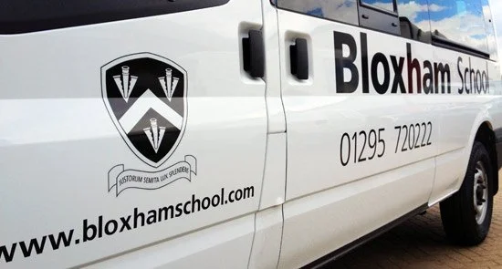 Side view of a white van with Bloxham School logo, website, and phone number printed on it.