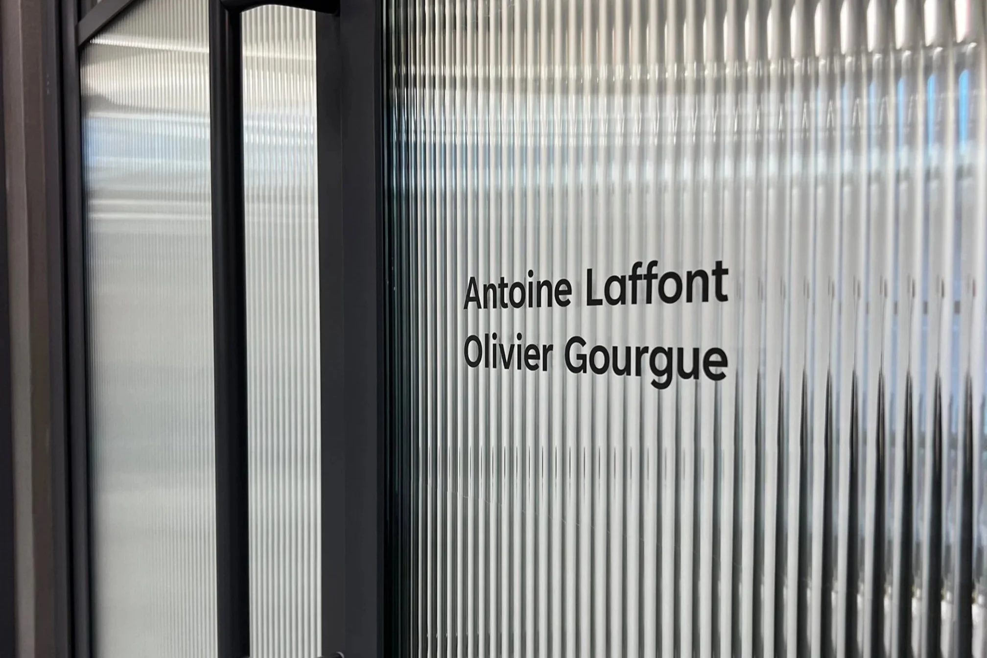 Glass door with vinyl black lettering displaying names. Office reeded window graphics.