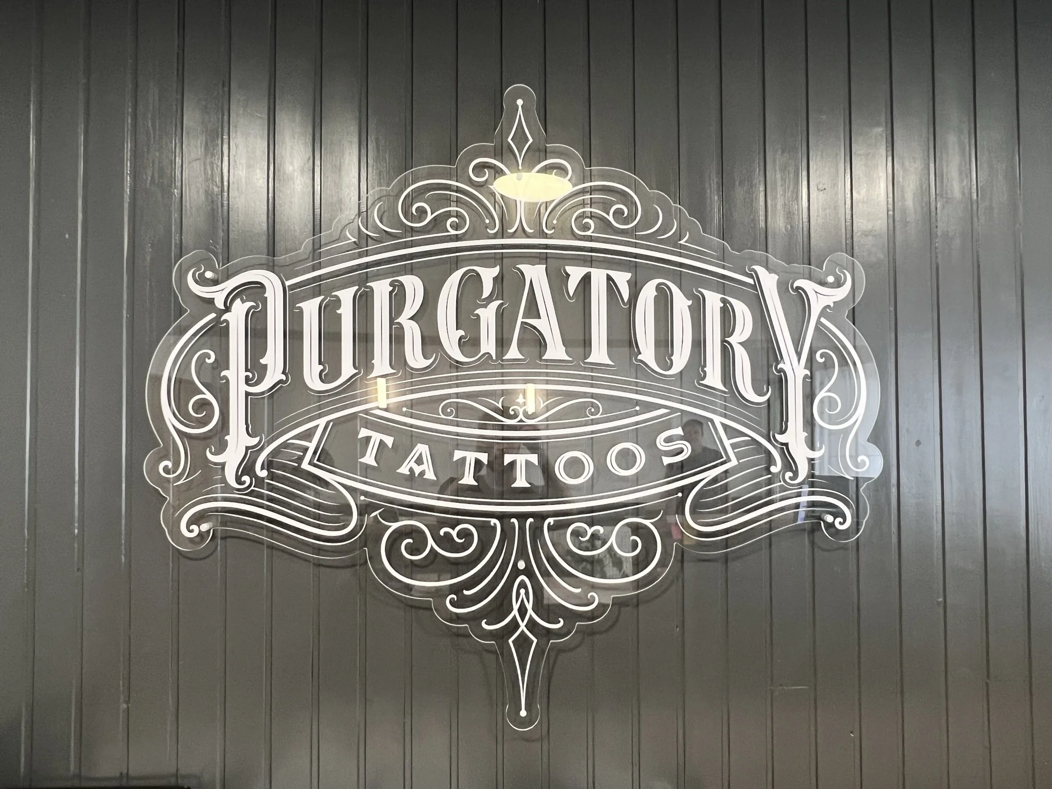 Decorative sign on dark wall for 'Purgatory Tattoos' shop.