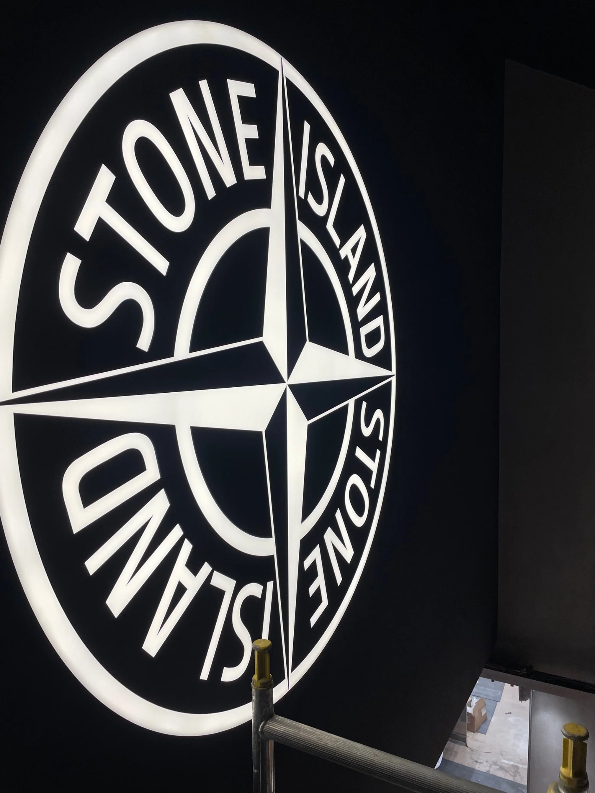 Backlit wall sign displaying the Stone Island logo with a compass design and the brand name