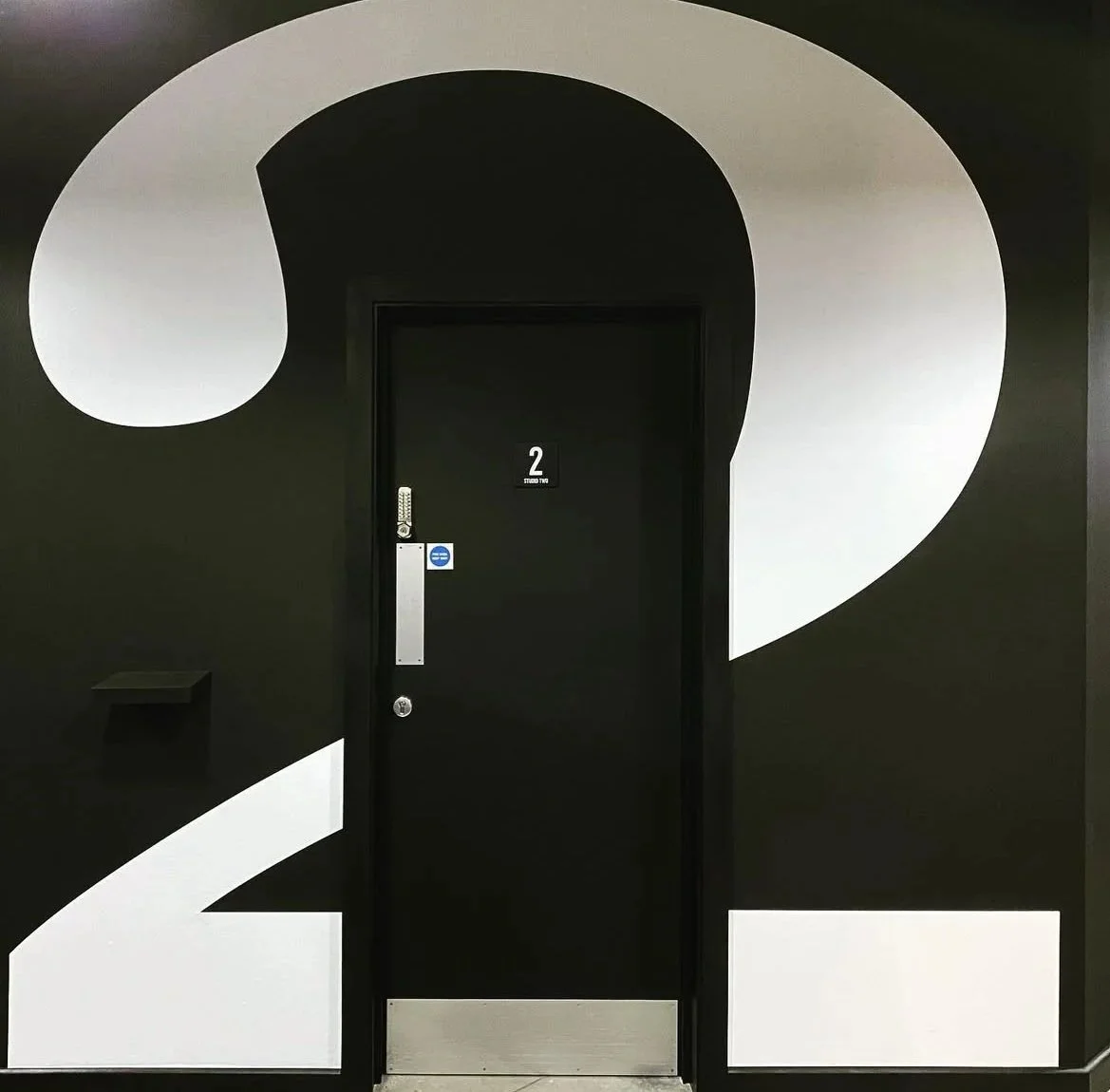 Black door with the number 2 and modern digital lock, surrounded by large white and black number 2s on the wall, creating a bold graphic design.