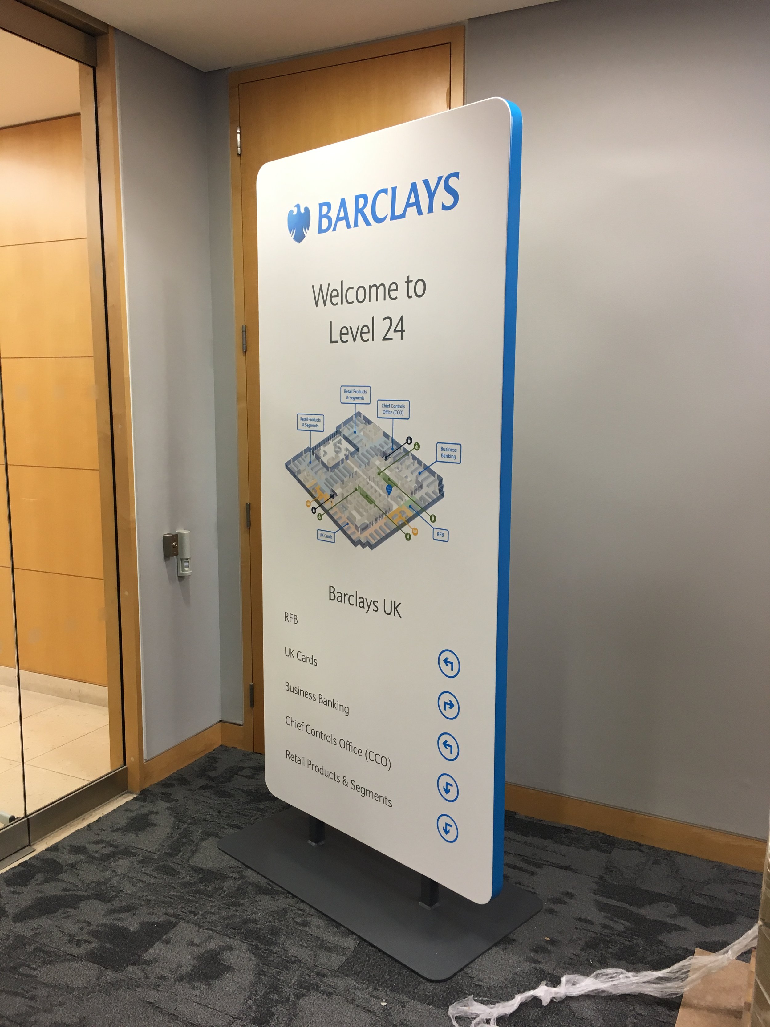A large vertical directory sign for Barclays Bank at Level 24, listing services like RFB, UK Cards, Business Banking, Chief Controls Office, and Retail Products & Segments, with floor plan diagram at the top.