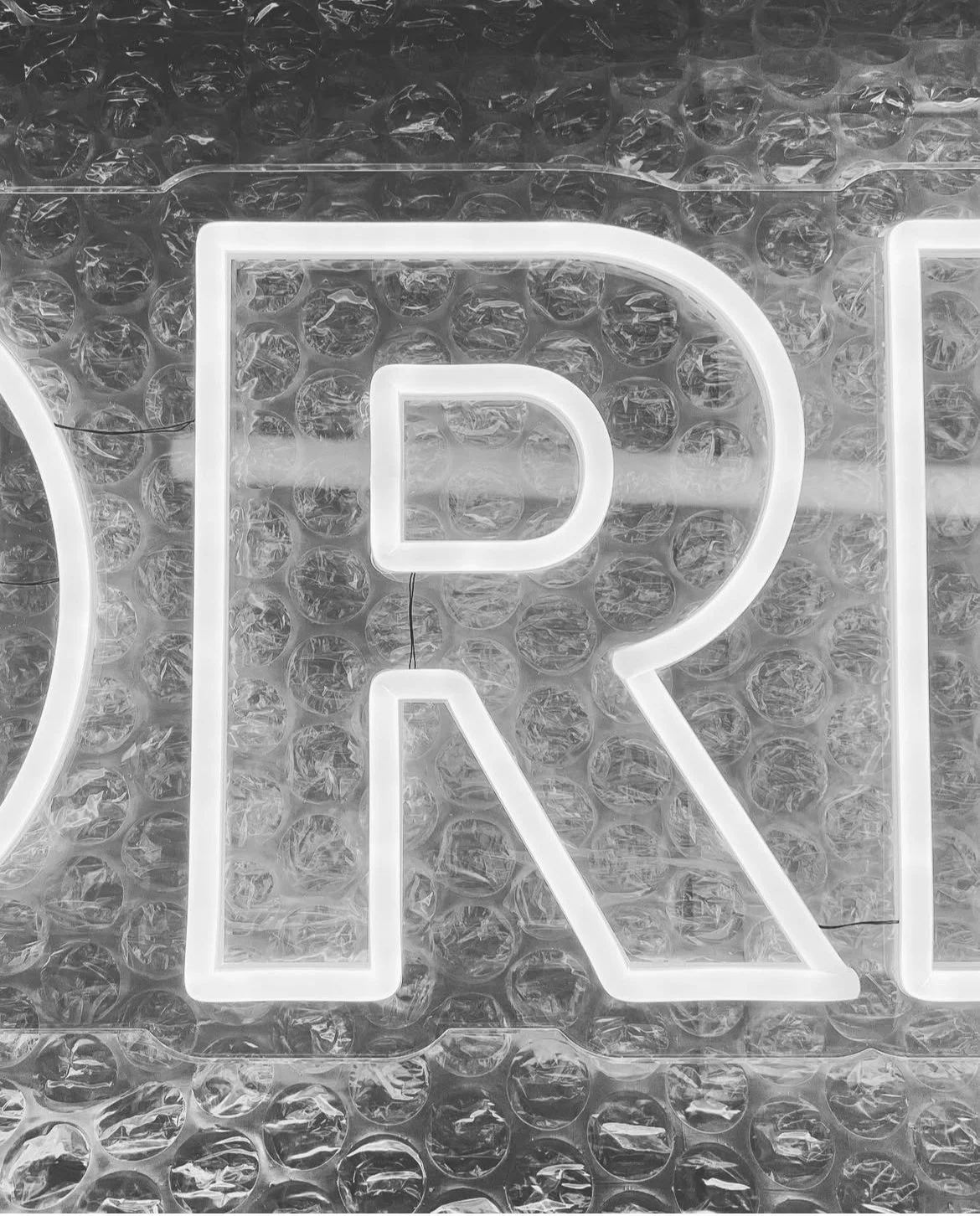 Close-up of a lit neon sign in the shape of the letter R, mounted on bubble wrap background.