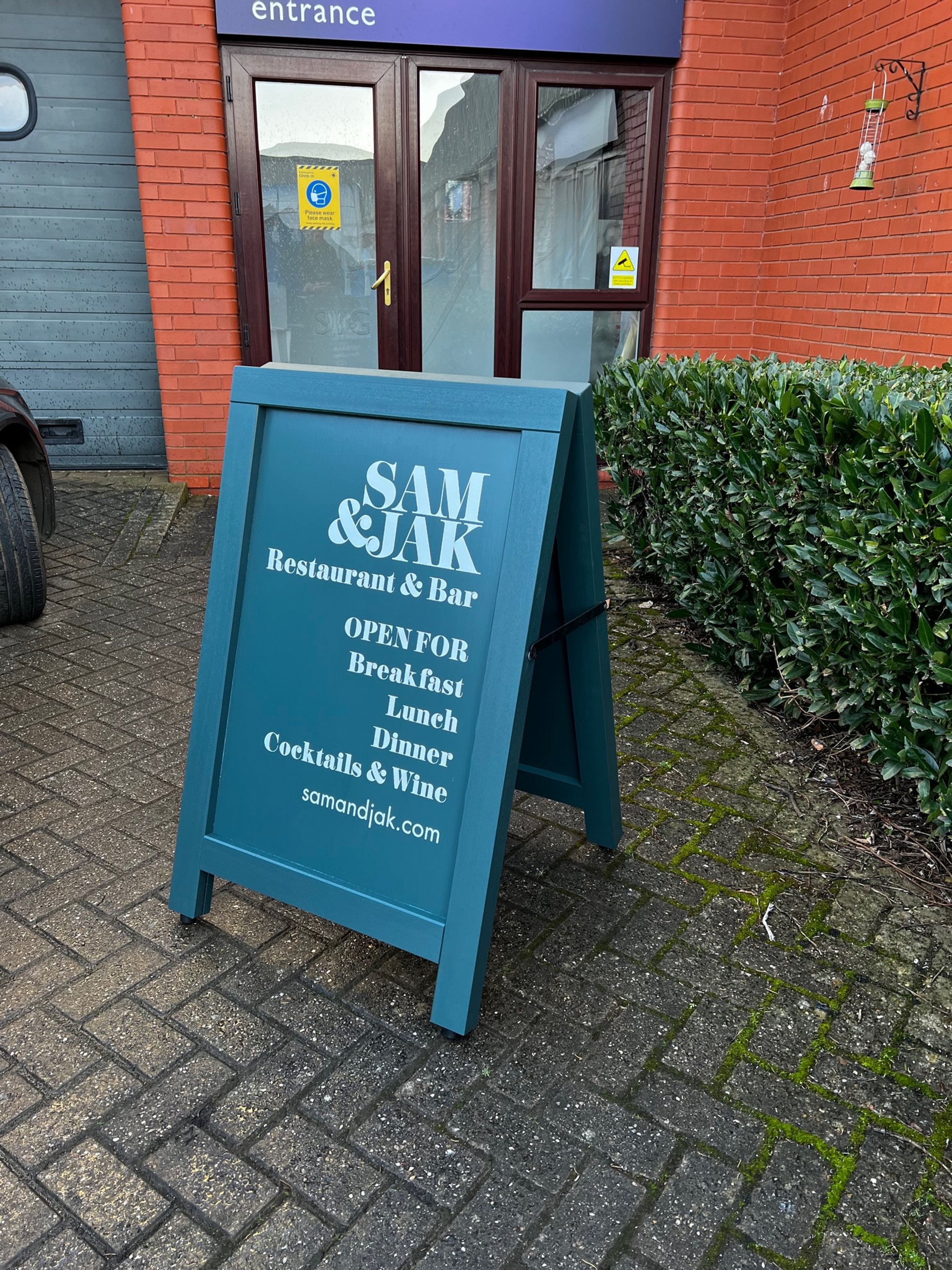Blue sandwich board sign outside a restaurant called Sam & Jack Restaurant & Bar, advertising breakfast, lunch, dinner, cocktails, and wine, with the restaurant's website, samandjack.com.