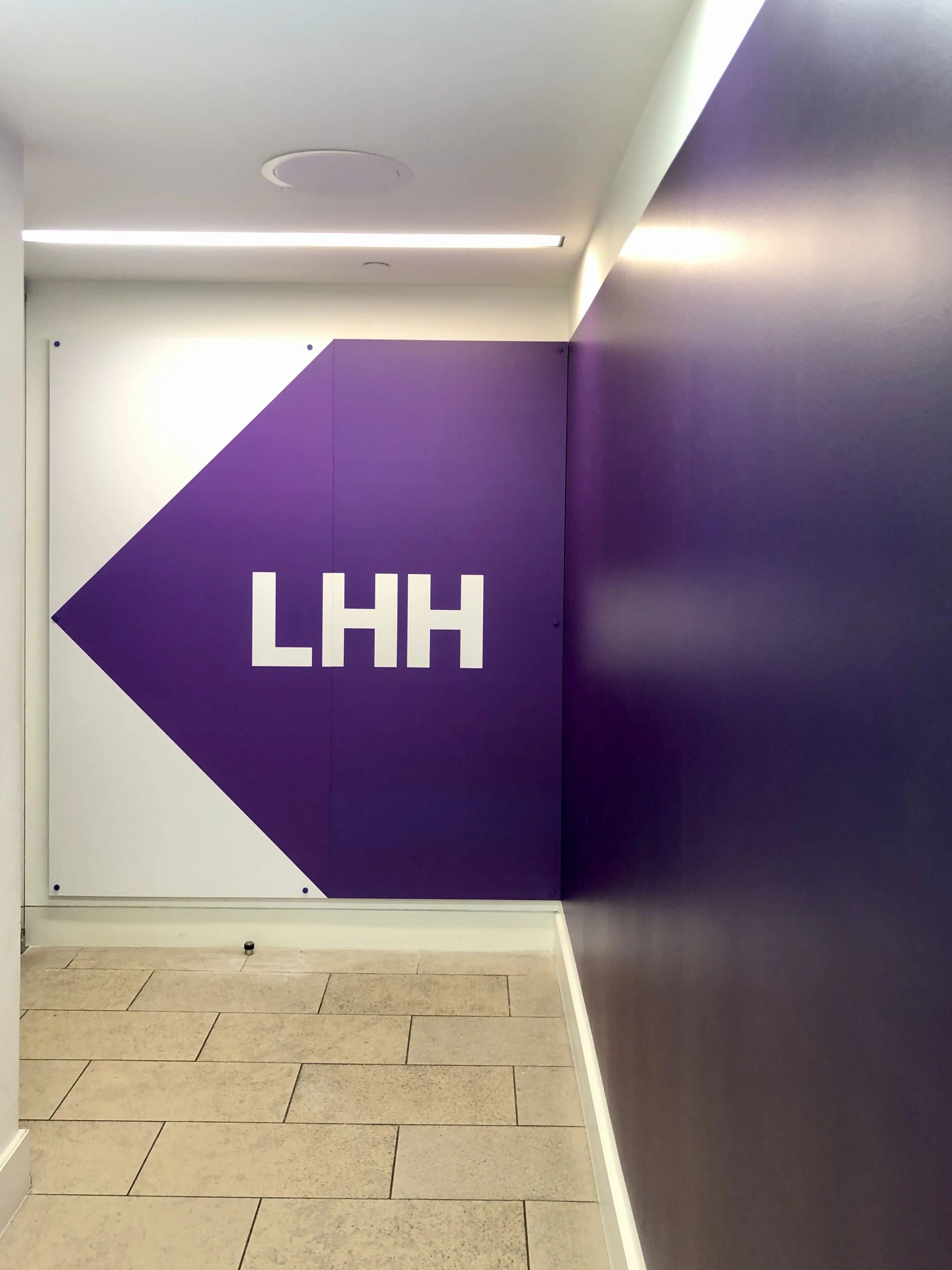 Purple and white directional sign with the letters 'LHH' pointing to the left.