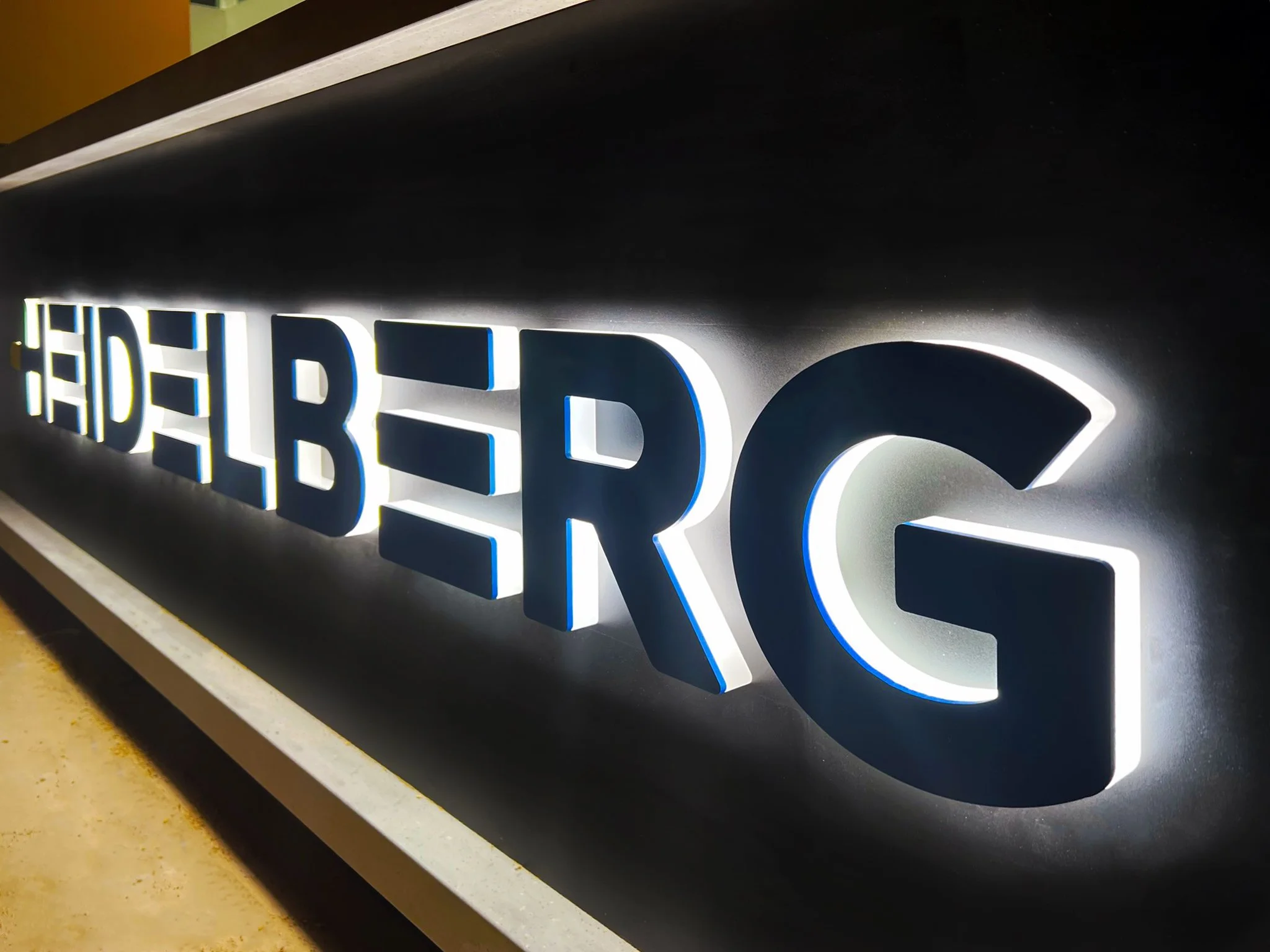 Illuminated sign displaying the text 'The Deliberating' with backlit blue and white letters.