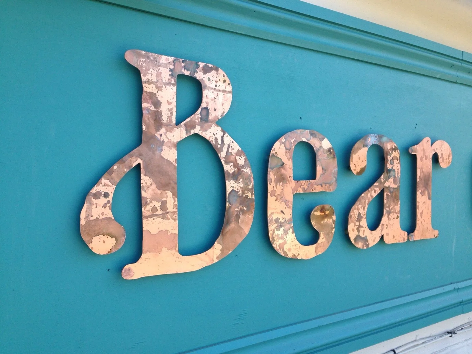 Metal sign spelling 'Dear' mounted on a teal wall.