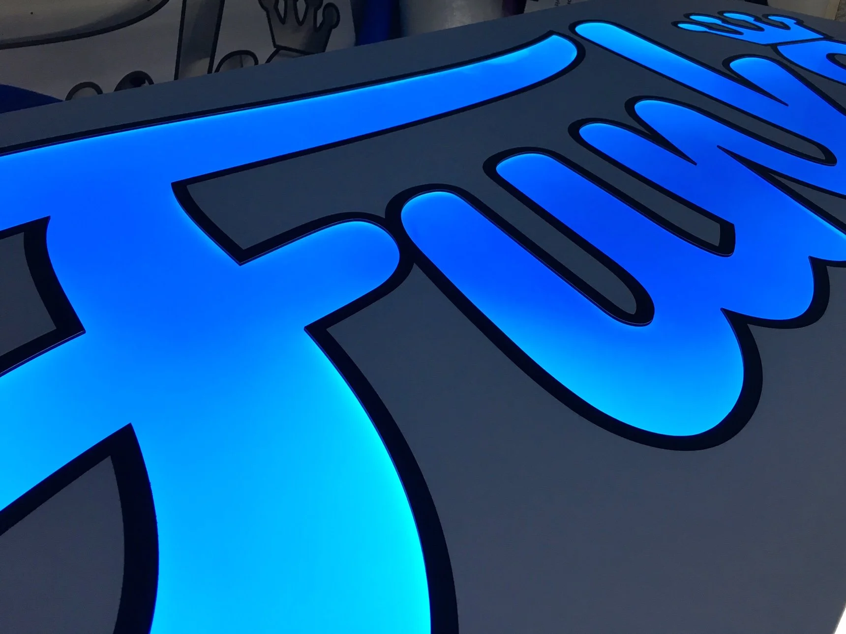 Close-up of a illuminated blue sign with large outlined lettering.