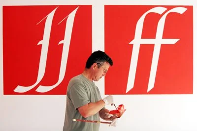 A man looking at his phone in front of a wall with large red and white lettered designs.
