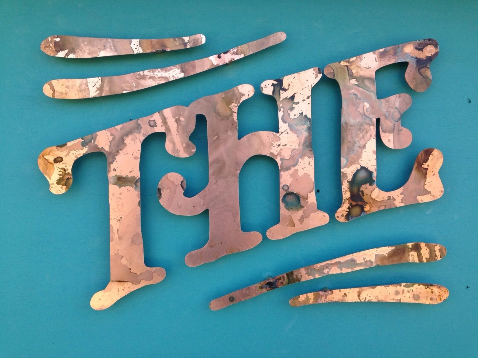 Metal art piece spelling out the word 'LOVE' with two horizontal lines above and below, mounted on a teal wall.