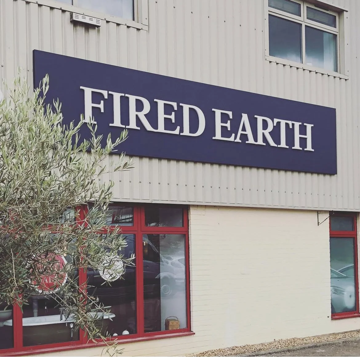 Building with a sign that reads "FIRE D EARTH" and windows with red frames, with a tree in front.