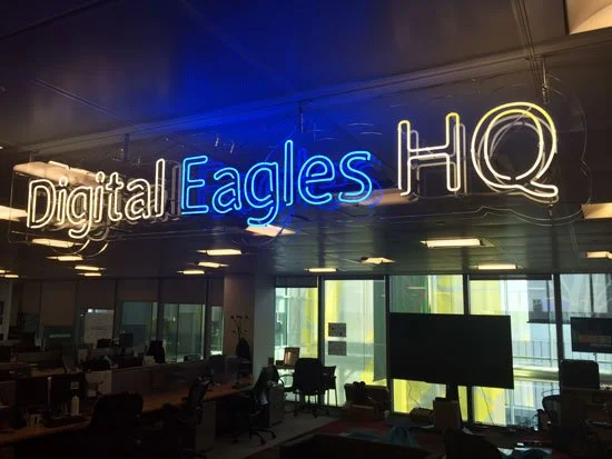 Neon sign reading 'Digital Eagles HQ' inside a modern office with desks and computers.
