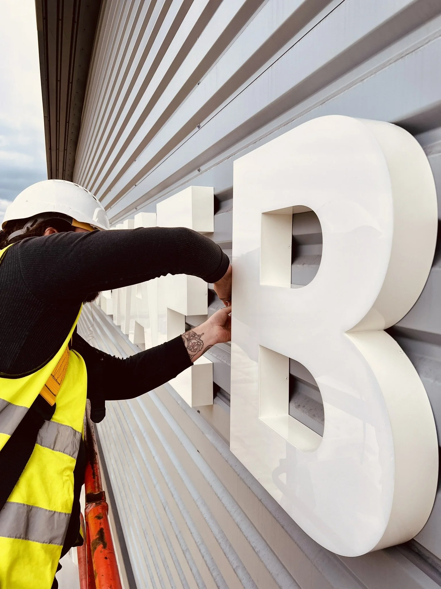 Worker installing large white letter 'B' onto building exterior.