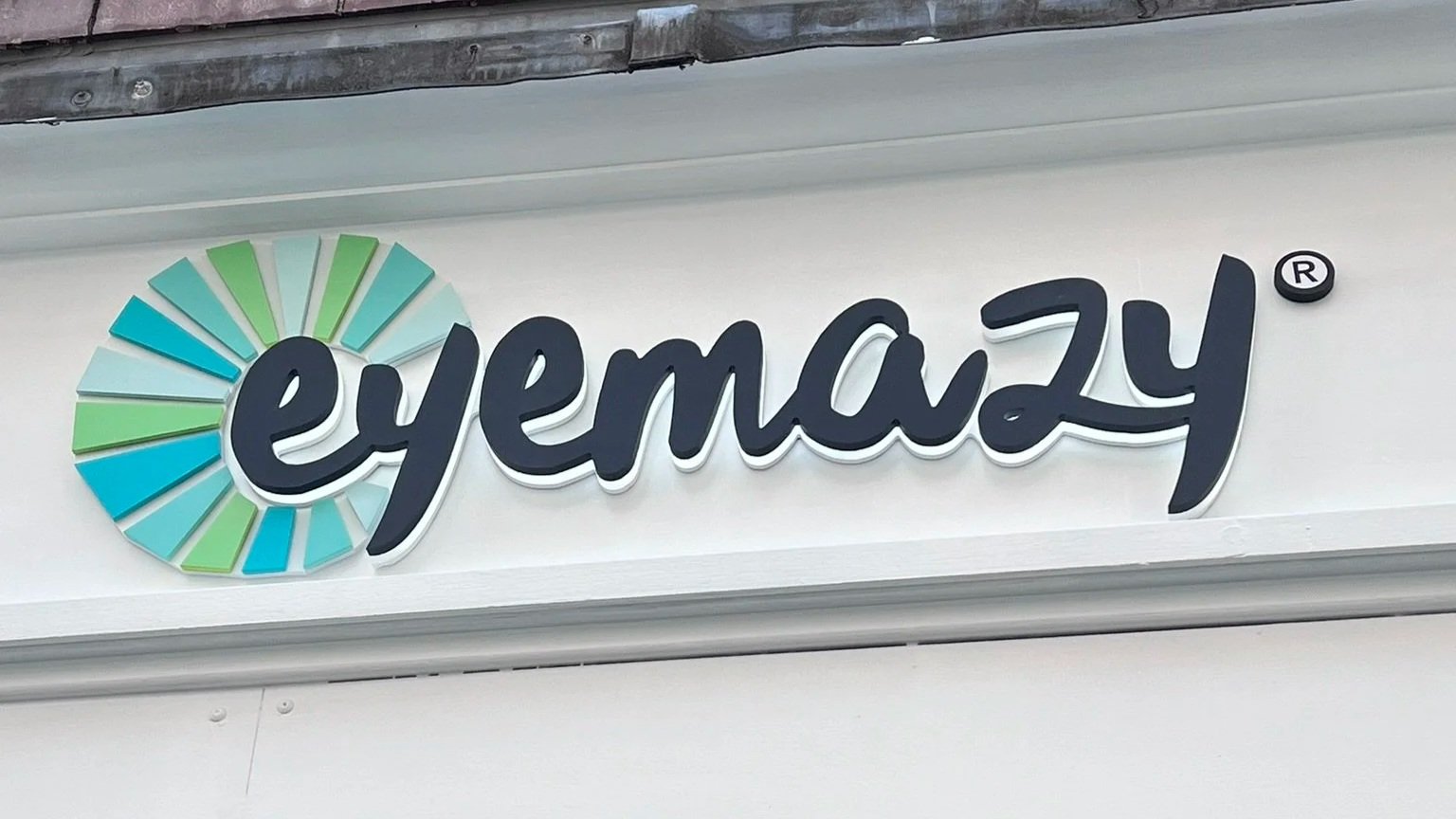 A sign with the eBay logo displaying the word 'eyemazy' in stylized cursive font next to a multicolored circular design.