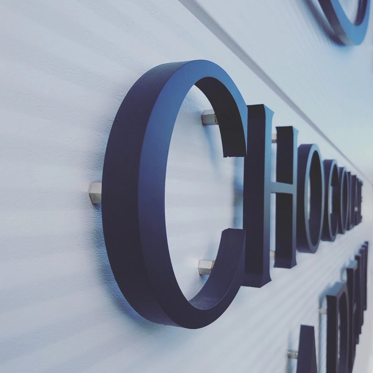 Close-up of black 3D letters mounted on a white textured wall, with a focus on the letter 'C'.