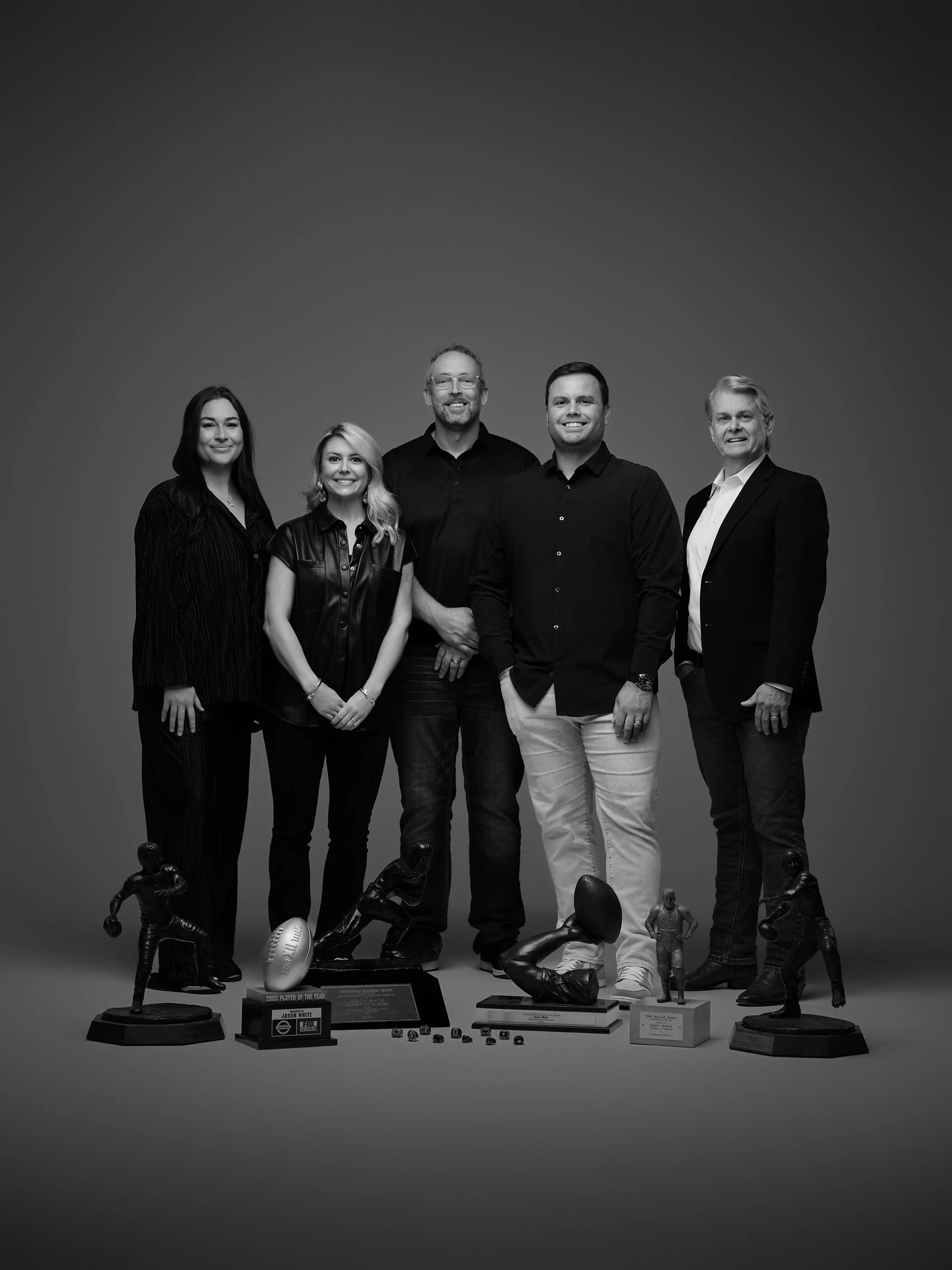 Group of five people standing behind sports trophies and awards on a plain background.
